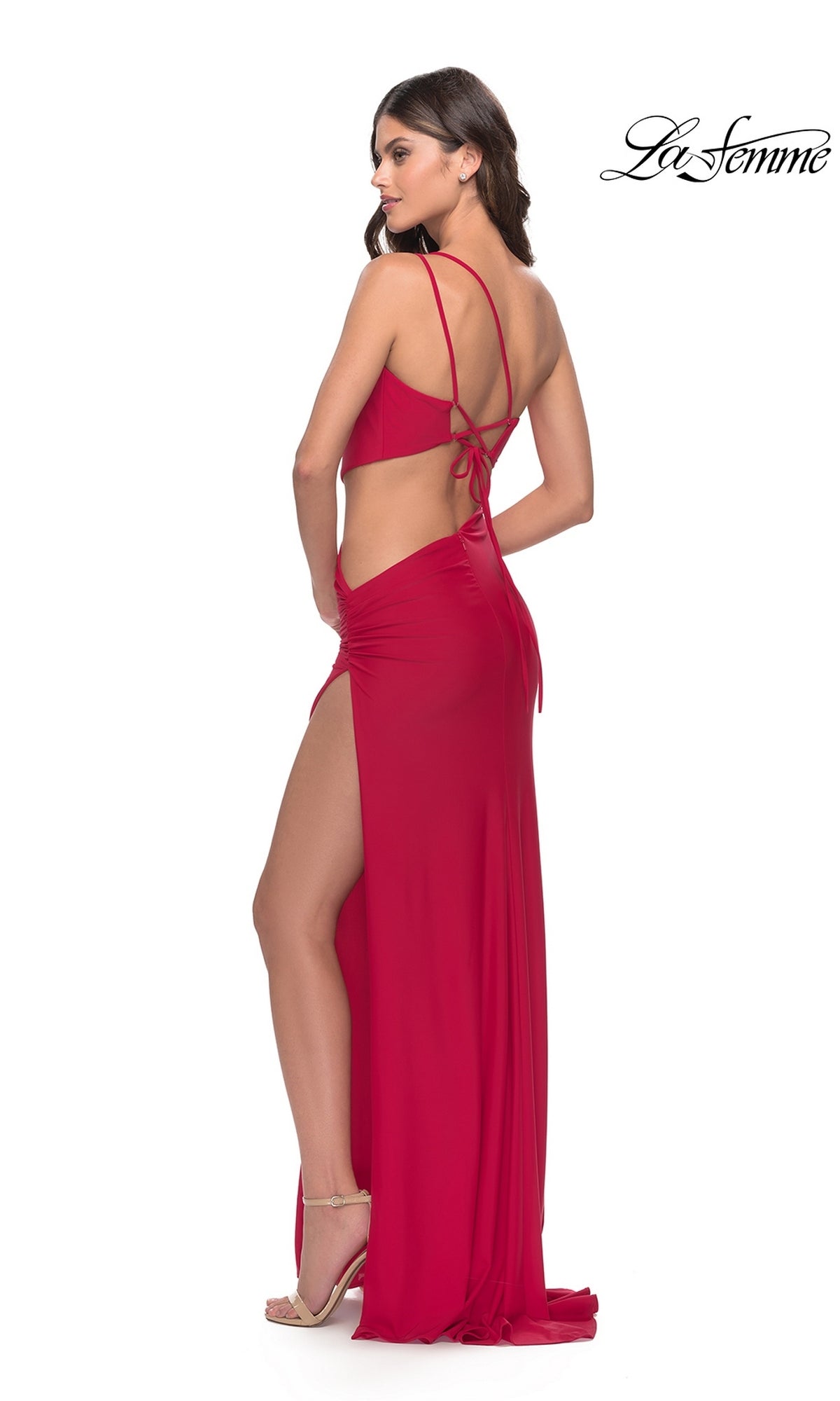 A woman wears a floor-length red Long Prom Dress: La Femme 31386 featuring a one-shoulder cutout, high side slit, and lace-up back detail.