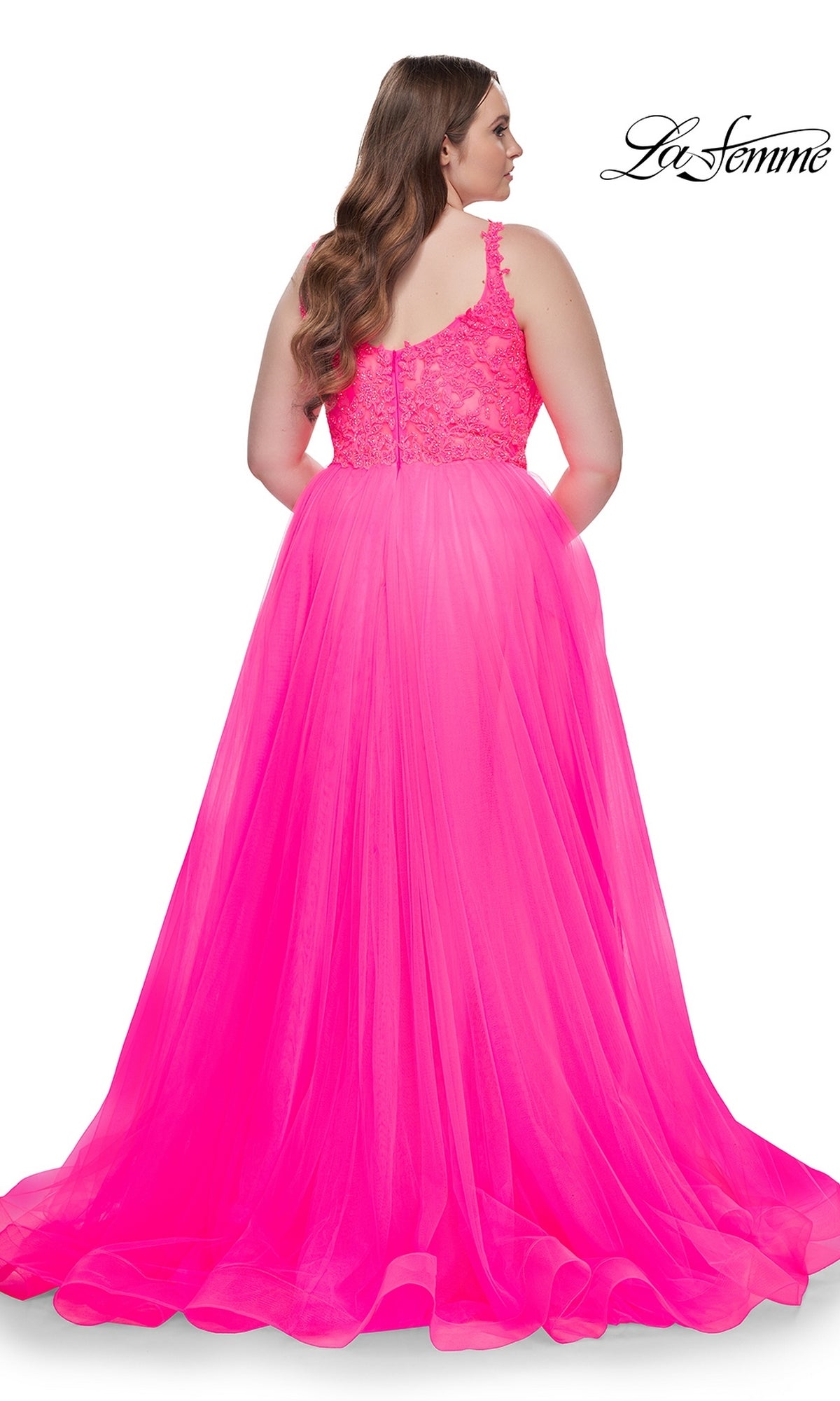 A woman with long brown hair wears the La Femme Long Prom Dress 31394, a sleeveless bright pink gown with an embroidered lace bodice and tulle skirt, shown from the back against a white background.