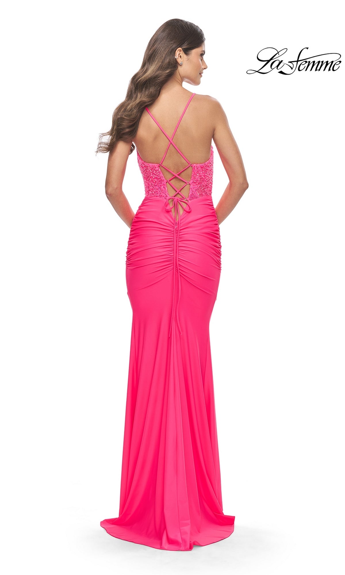 A woman faces away in a bright pink, floor-length Sheer-Corset Lace-Up Prom Gown: La Femme 31437 featuring a crisscross back and ruching detail; the