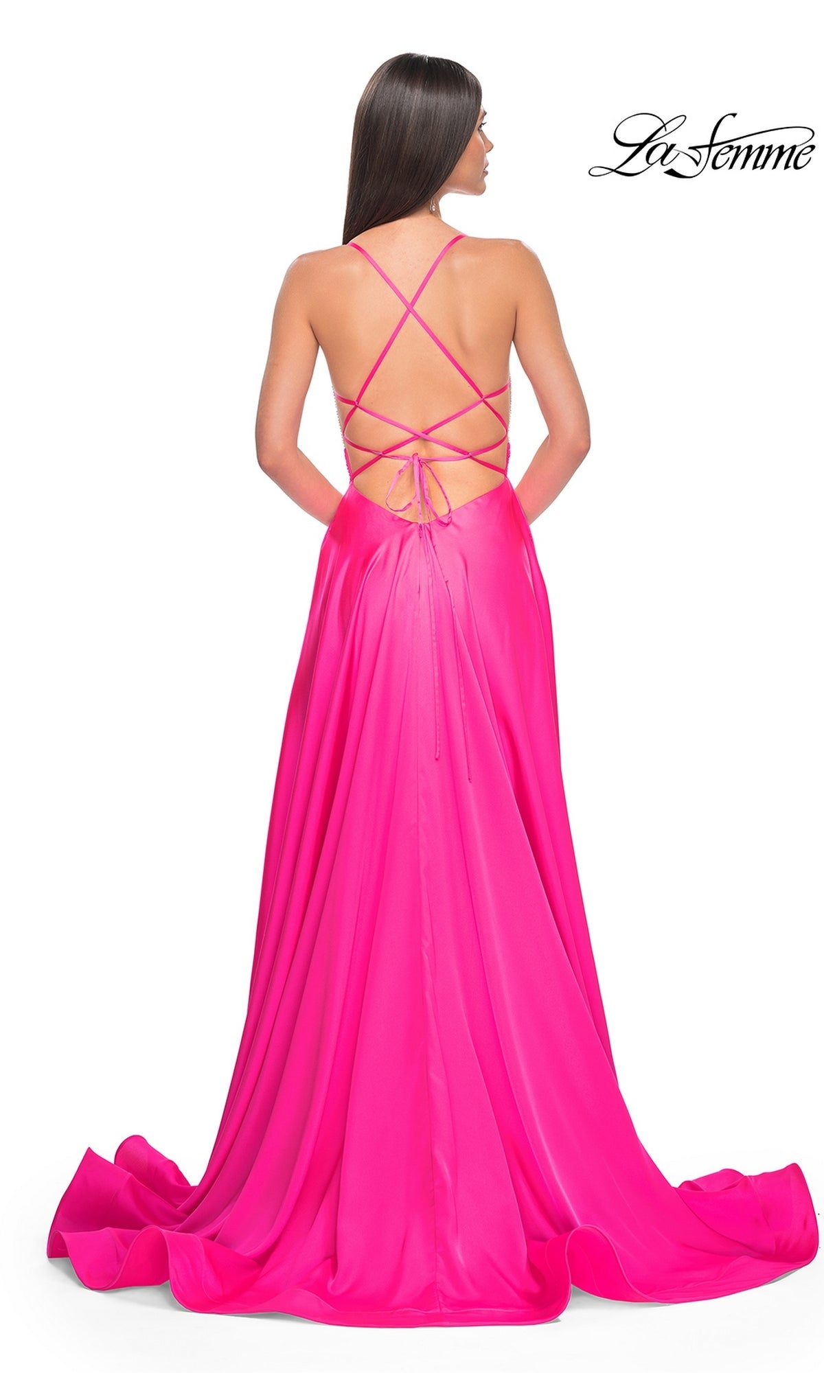 A woman with straight brown hair wears the La Femme Neon Pink Long Prom Dress 31448, featuring a beaded bodice, crisscross open back, and flowing floor-length train.