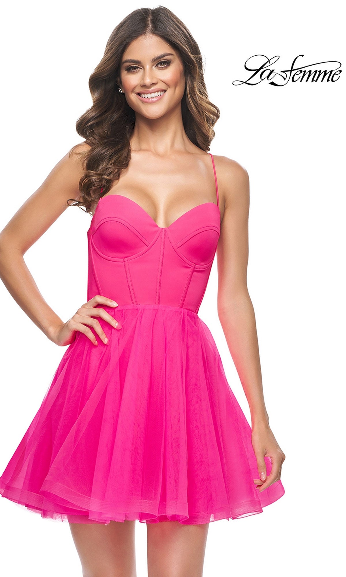 A woman wearing the Hot Pink Short La Femme Homecoming Dress 31468, featuring a satin corset bodice and fitted silhouette, smiles against a white background with the