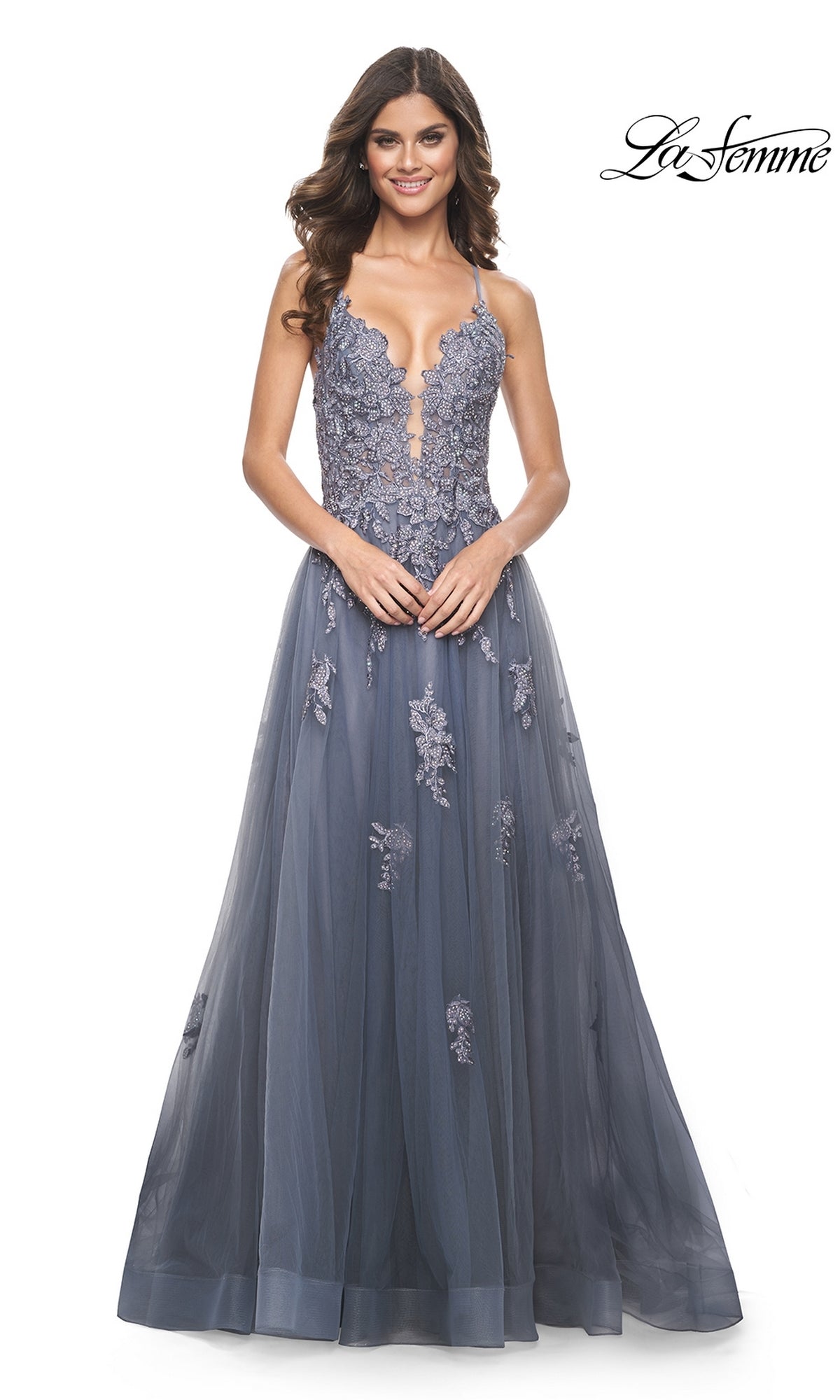 A woman faces forward in the La Femme Plunging V-Neck Long Prom Ball Gown 31472, a sleeveless, floor-length slate blue dress with an embroidered lace appliqué bodice and tulle skirt. The La Femme logo is in the top right corner.