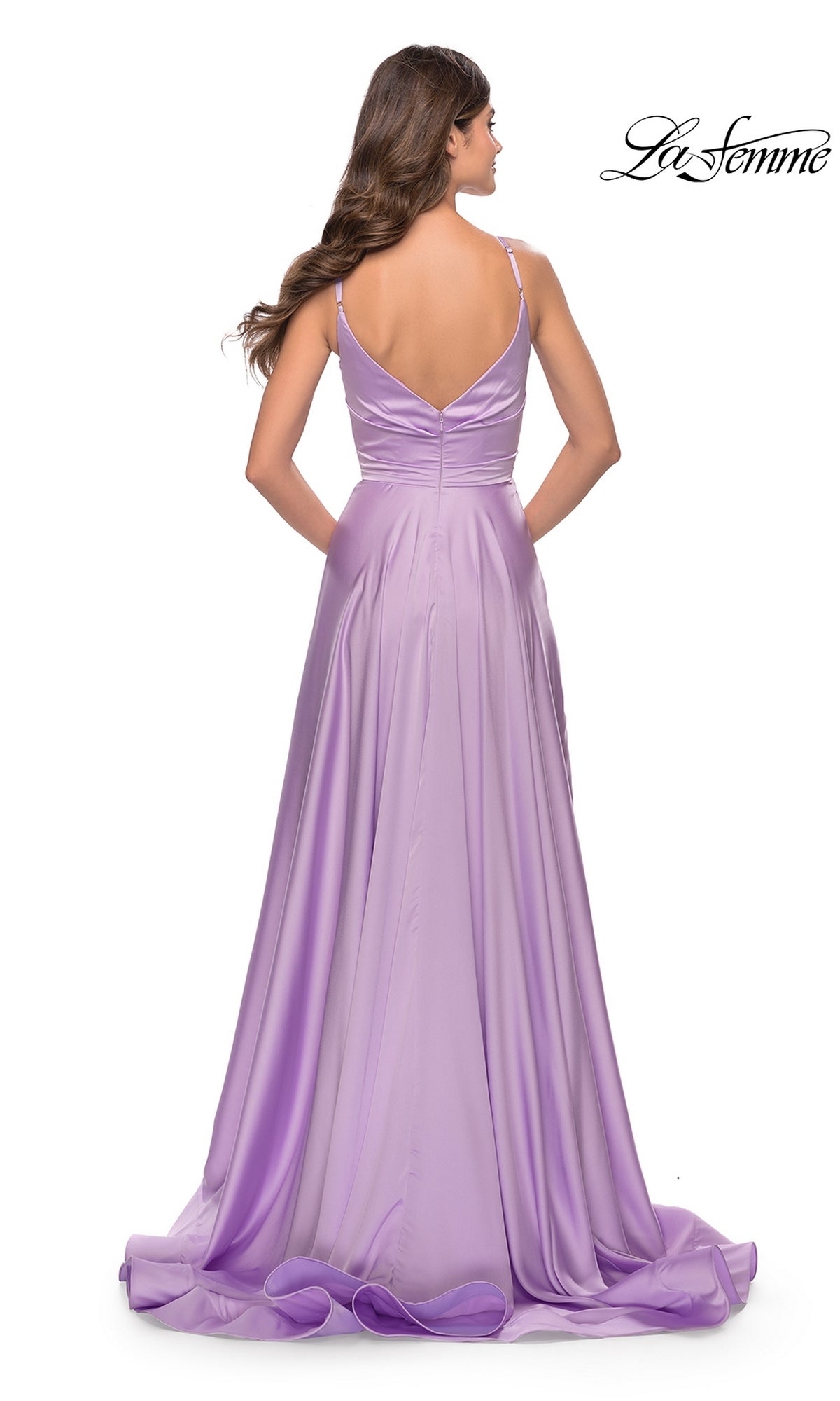 A woman with long brown hair stands against a white background, wearing the La Femme V-Neck Long A-Line Prom Dress 31505, a floor-length lavender satin gown with thin straps and a V-shaped back.