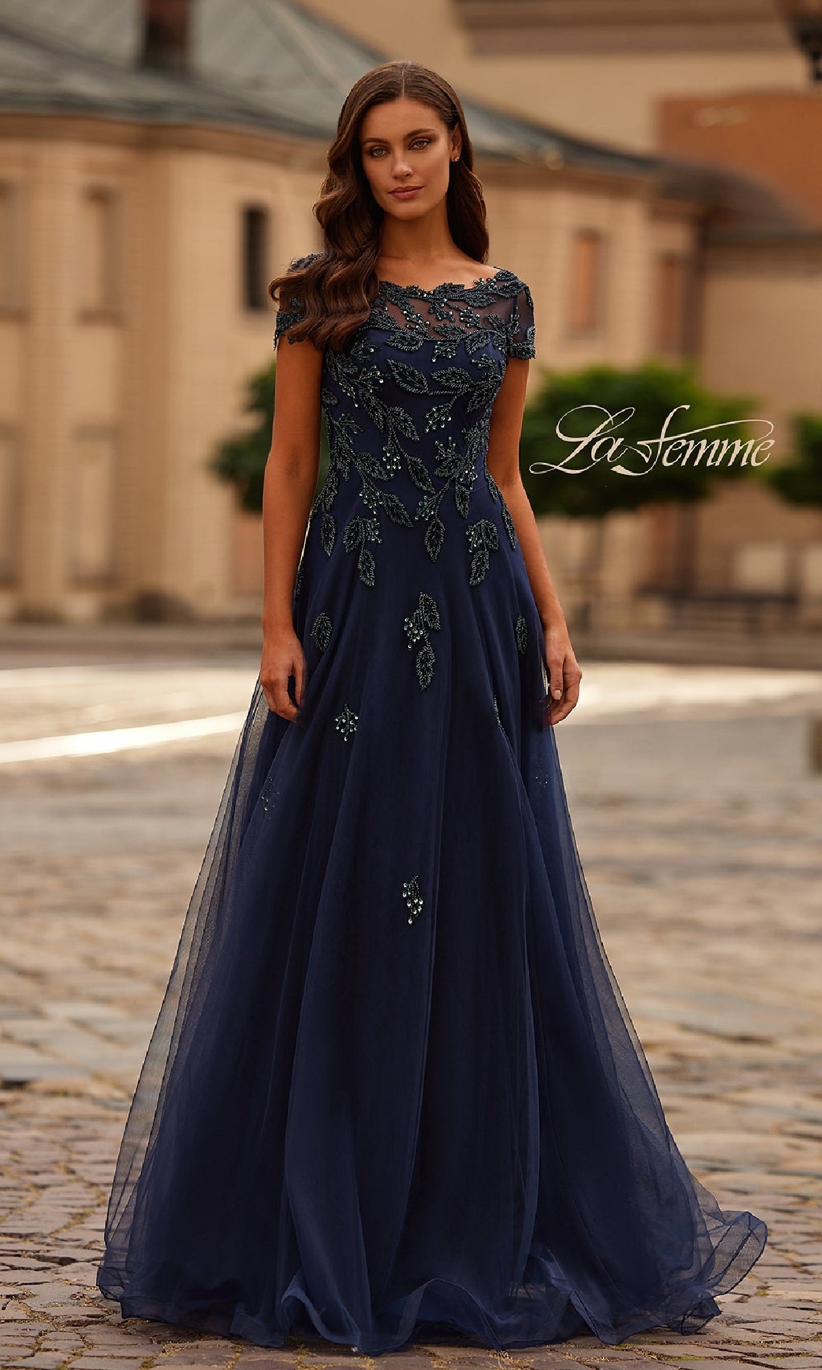 A woman stands outdoors wearing the La Femme 31692 navy formal dress, featuring short sleeves and beaded floral embellishments.