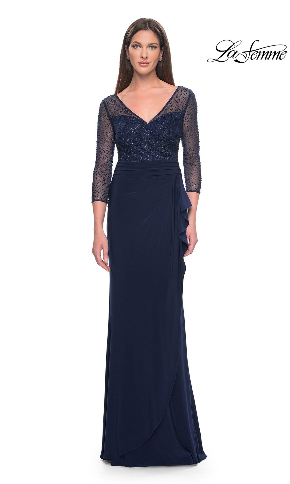 The La Femme 31777 is a navy blue long jersey formal dress featuring a V-neck bodice, three-quarter length sleeves, a sheer beaded overlay, and a draped skirt with a side ruffle.