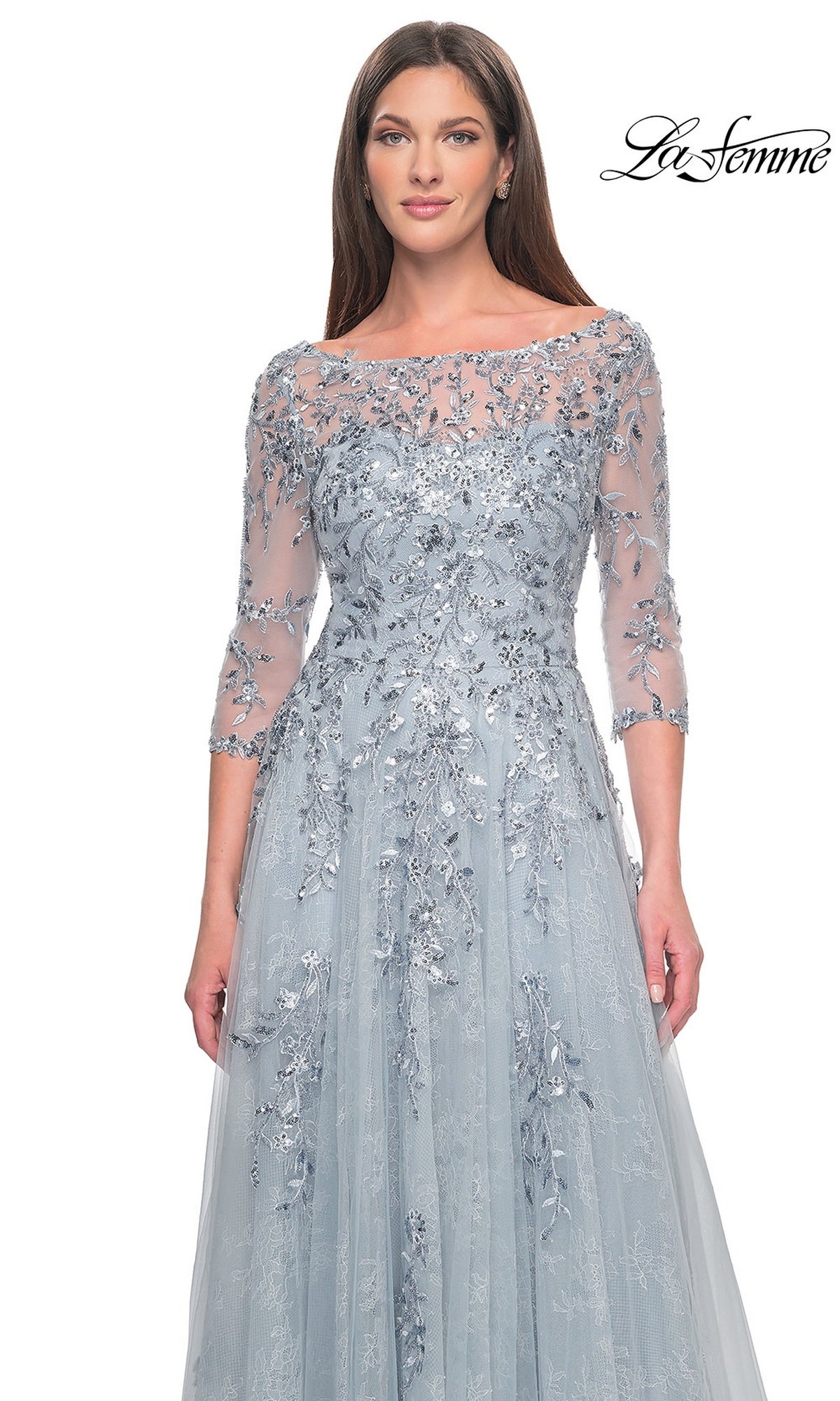 A model wears the Long Formal Dress: La Femme 31795, a dusty blue floor-length gown with three-quarter sleeves, a boat neckline, and intricate silver floral embroidery and sequins throughout.
