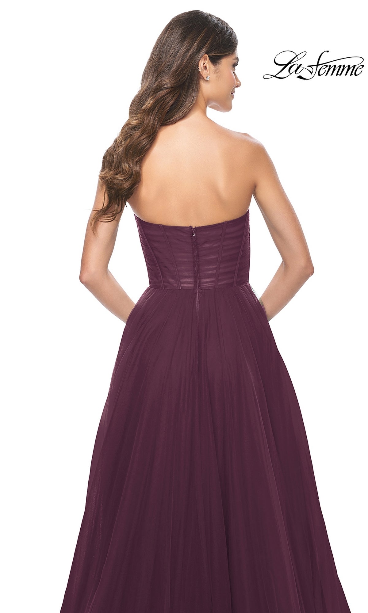 A woman with long brown hair elegantly models the La Femme Strapless Long A-Line Prom Dress 31971 in burgundy, featuring a fitted bodice and floor-length skirt, seen from the back.