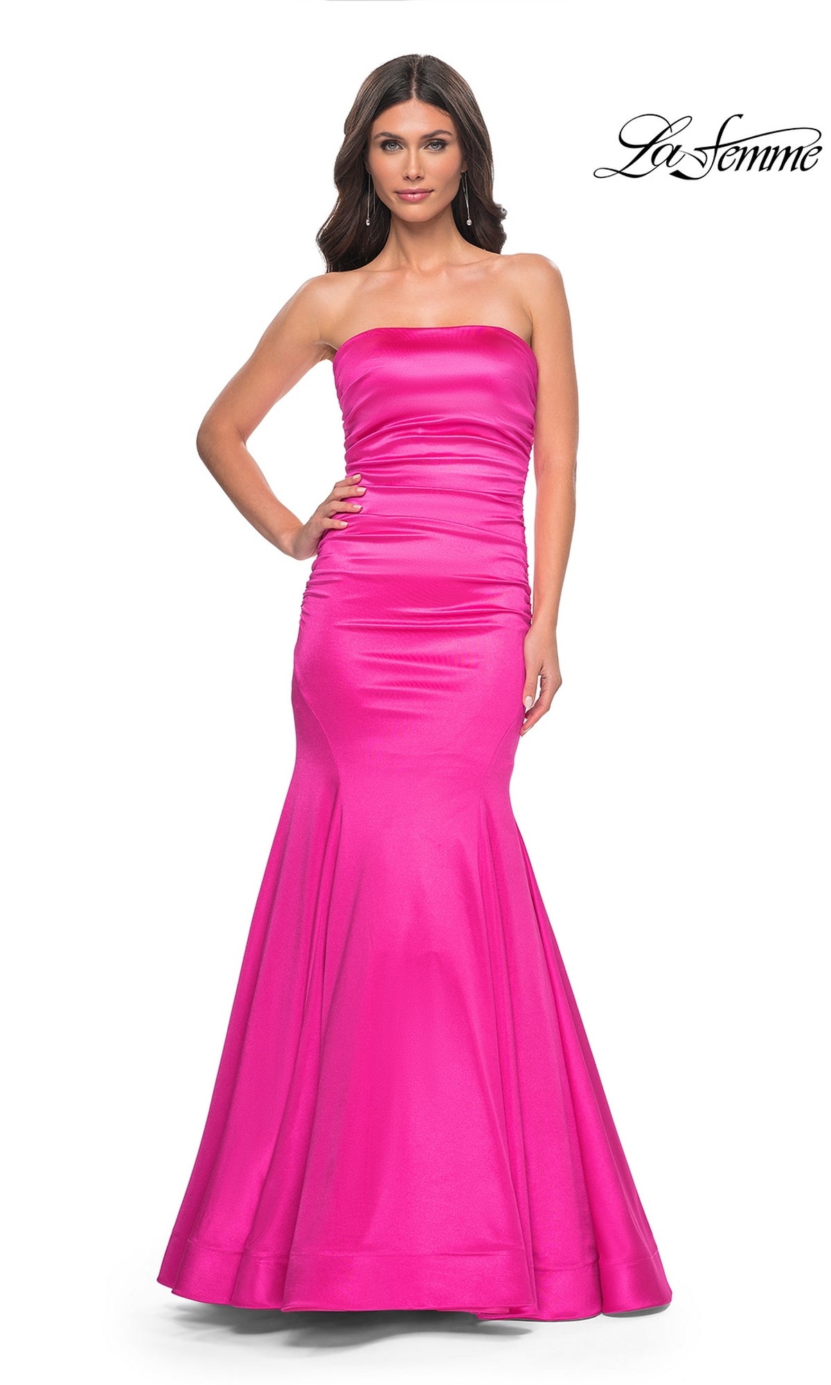 A woman models the La Femme Strapless Long Mermaid Prom Dress 31980 in bright pink. This smooth, shiny gown features slight ruching on the bodice and a dramatic flared hem for a stunning formal look.