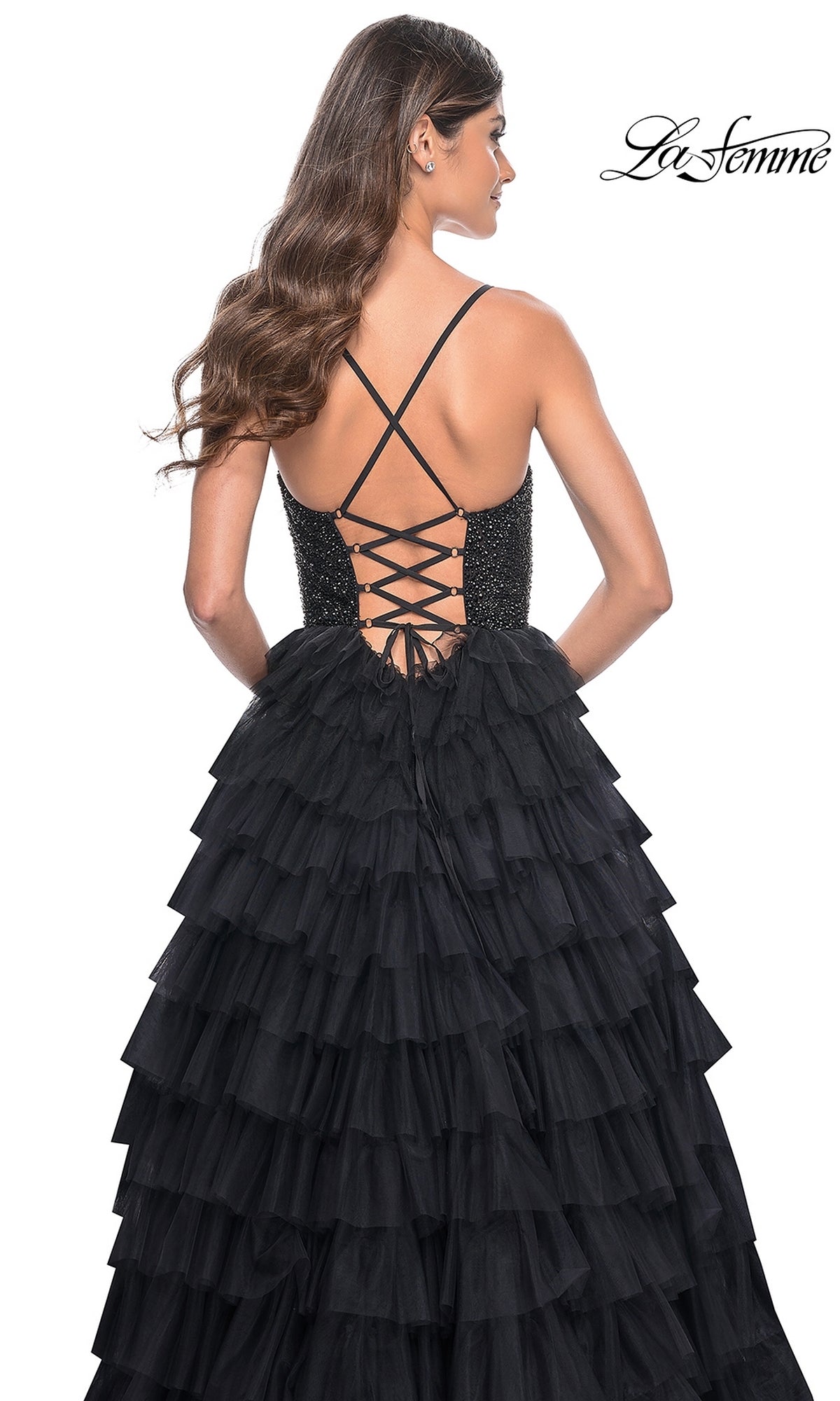 A woman wears the La Femme Long Ruffled Prom Ball Gown 32002, a black A-line designer dress with thin straps, a lace-up back, fitted bodice, and voluminous ruffled skirt. The La Femme logo appears in the top right corner.