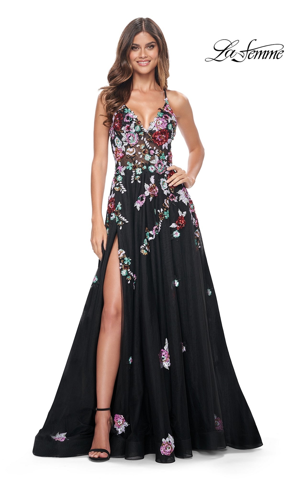 Smiling woman in the La Femme Floral-Sequin Long Black Prom Dress 32051, featuring colorful embroidered sequin flowers, thin straps, and a thigh-high slit, standing against a white background.