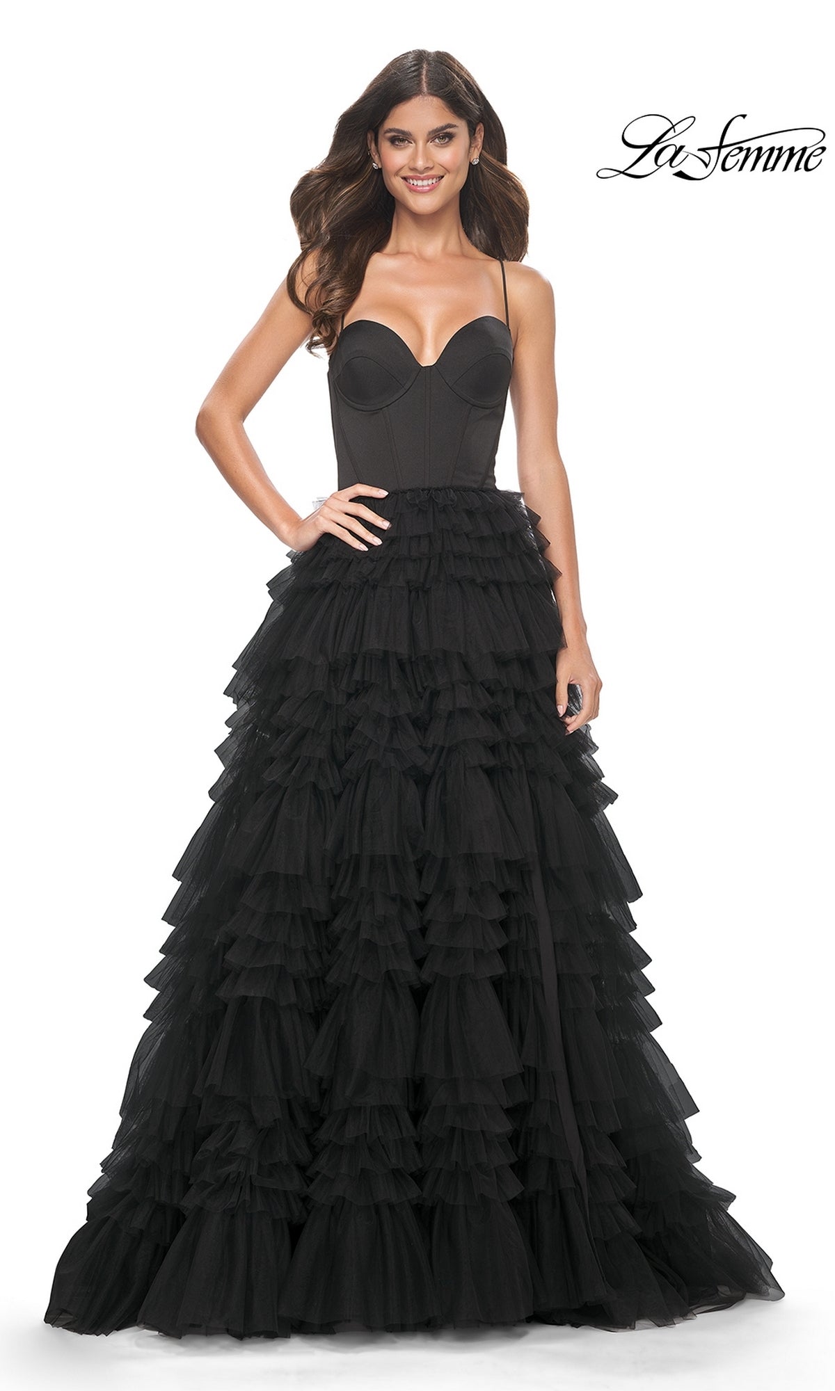 A woman stands smiling in the La Femme 32071 Lace-Up Ruffle Long Prom Ball Gown, featuring a strapless fitted bodice and layered tulle A-line skirt.