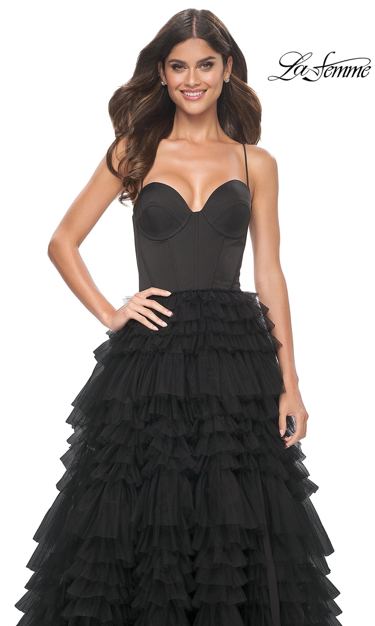 Woman wearing the Lace-Up Ruffle Long Prom Ball Gown: La Femme 32071, featuring a black strapless sweetheart corset bodice and layered ruffled tulle skirt, standing and smiling against a white background with
