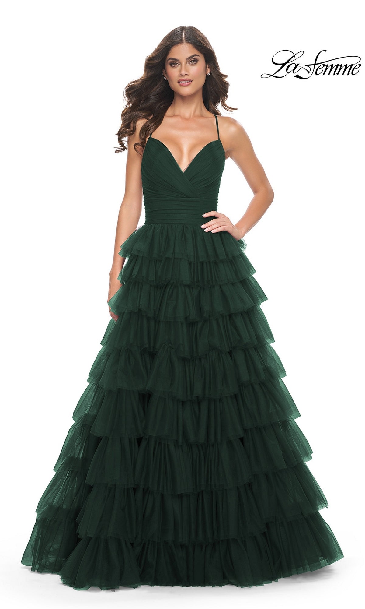 A woman wearing the La Femme Lace-Up Long Tiered Prom Dress 32086 in dark green, featuring spaghetti straps, stands against a white background.
