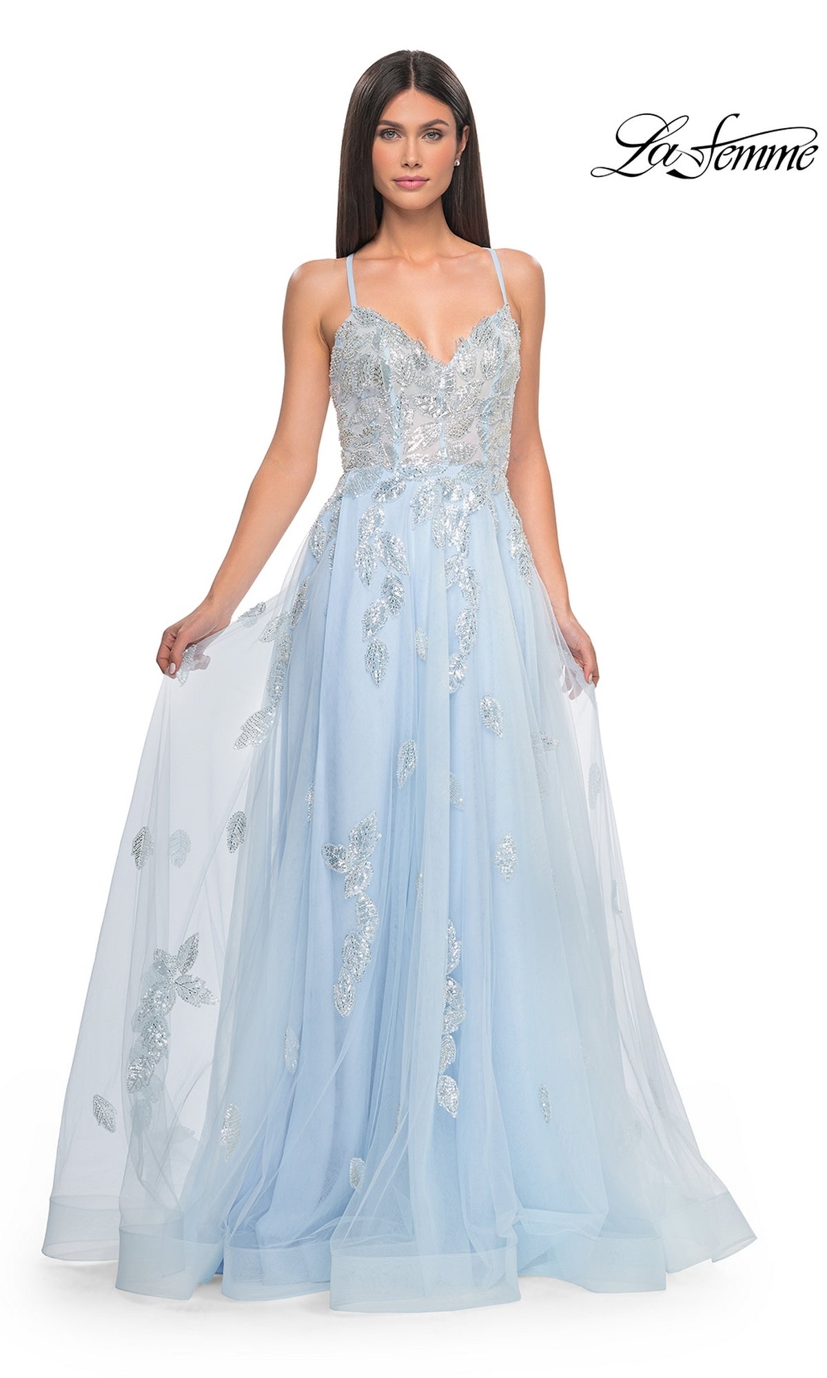 A woman models the La Femme Sequin-Embroidered Long Prom Dress 32090—a light blue, floor-length A-line gown with thin straps and silver sequin details—against a white background. The