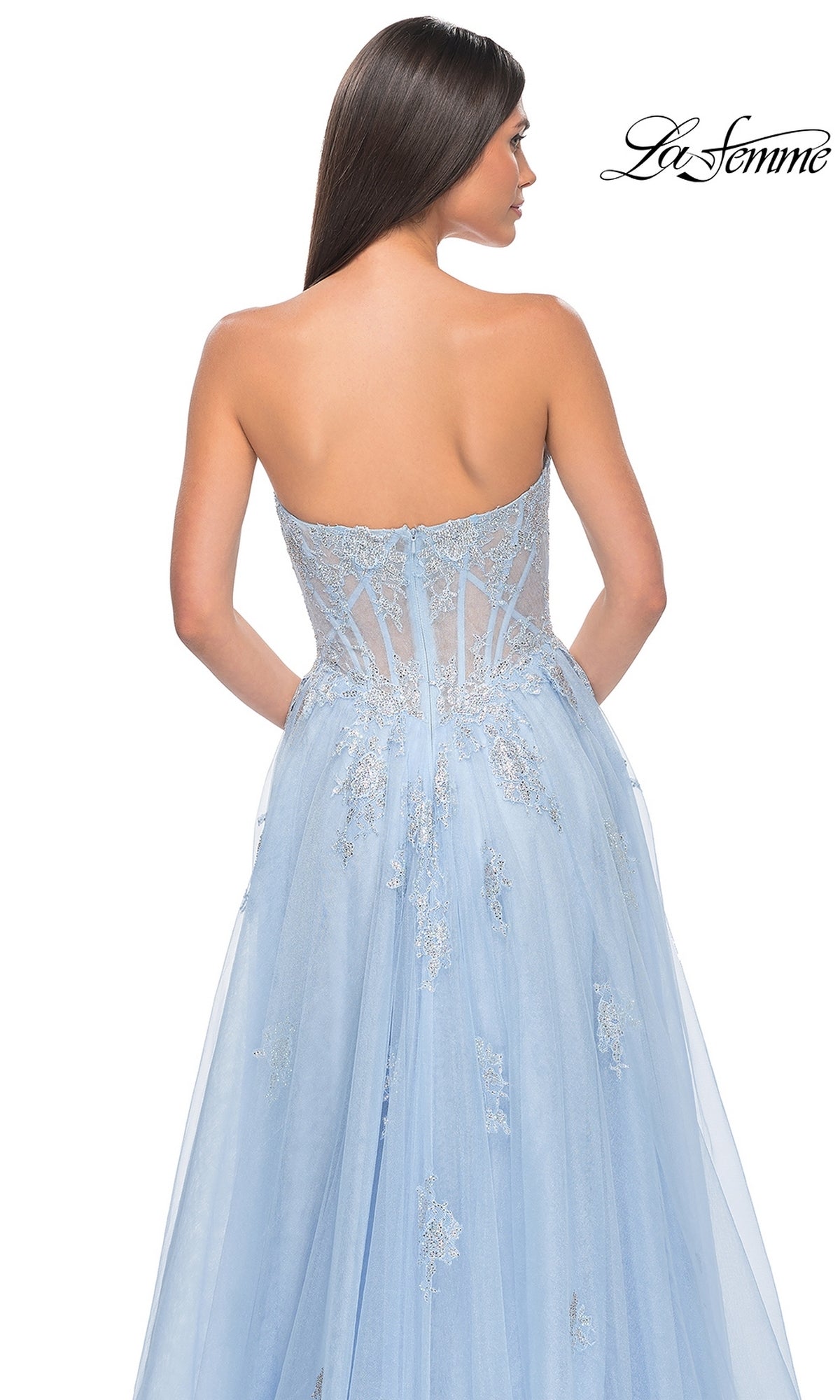 A woman with long dark hair models the La Femme Strapless Long A-Line Prom Dress 32111 in light blue, showcasing a sheer corset bodice and embroidered lace appliques from the back. The La Femme logo is displayed in the top right corner.