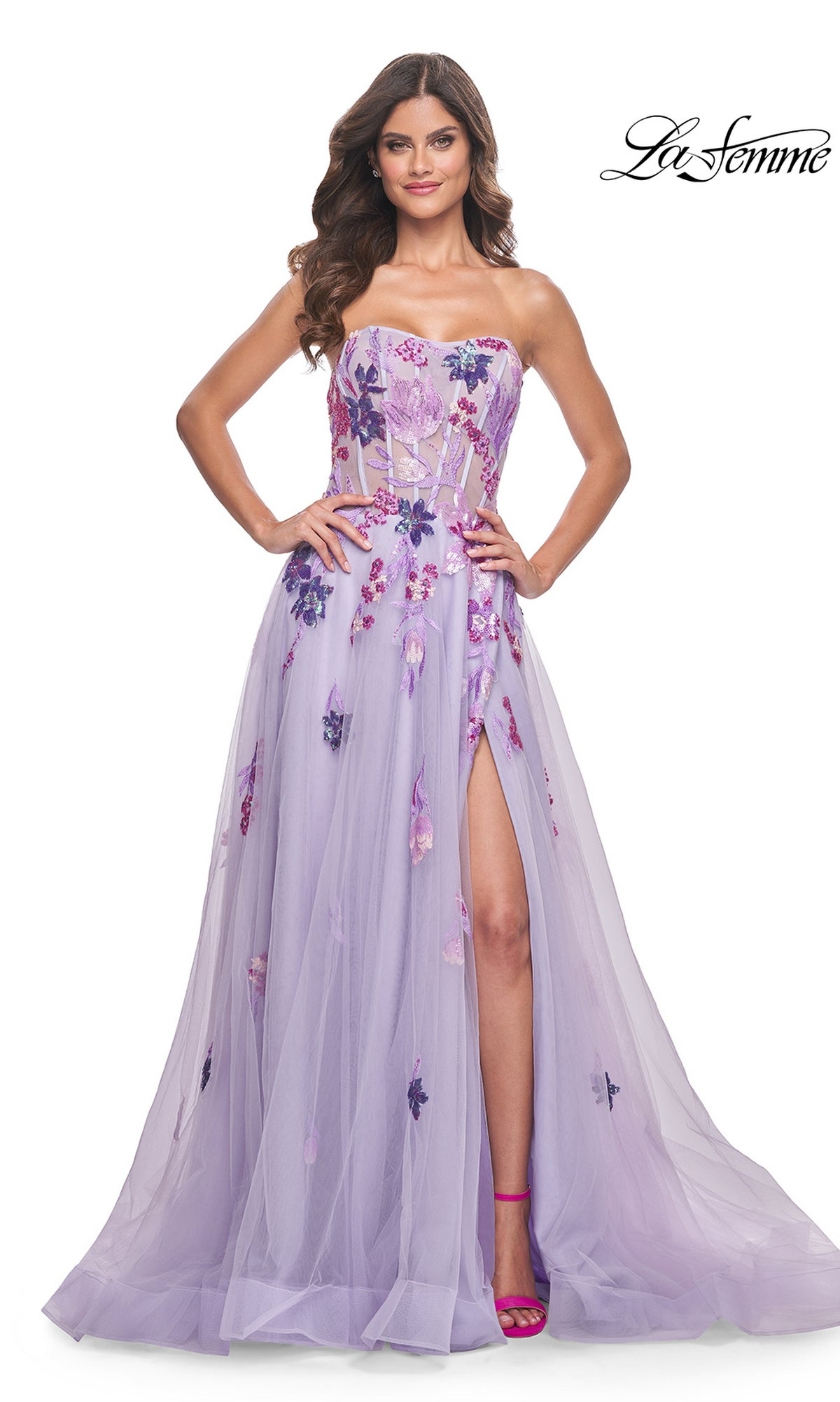 A woman poses with hands on hips against a white background, showcasing the La Femme Strapless Long Lavender Prom Dress 32156 featuring floral appliqué, a sheer bodice, and a thigh-high slit.