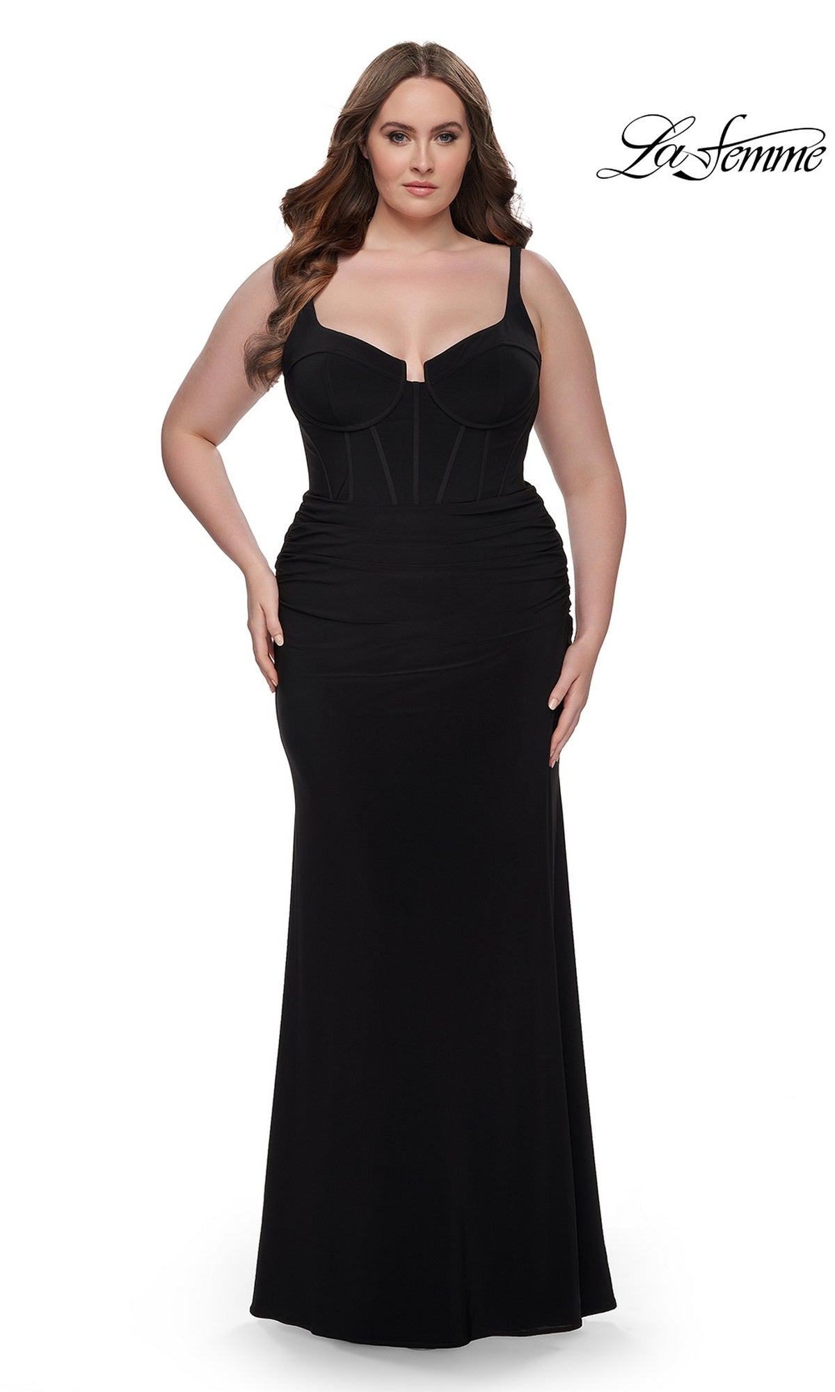 A woman in the La Femme Plus-Size Long Lace-Up Prom Dress 32190, a form-fitting black gown with a structured bodice and ruched details, stands against a white background. The