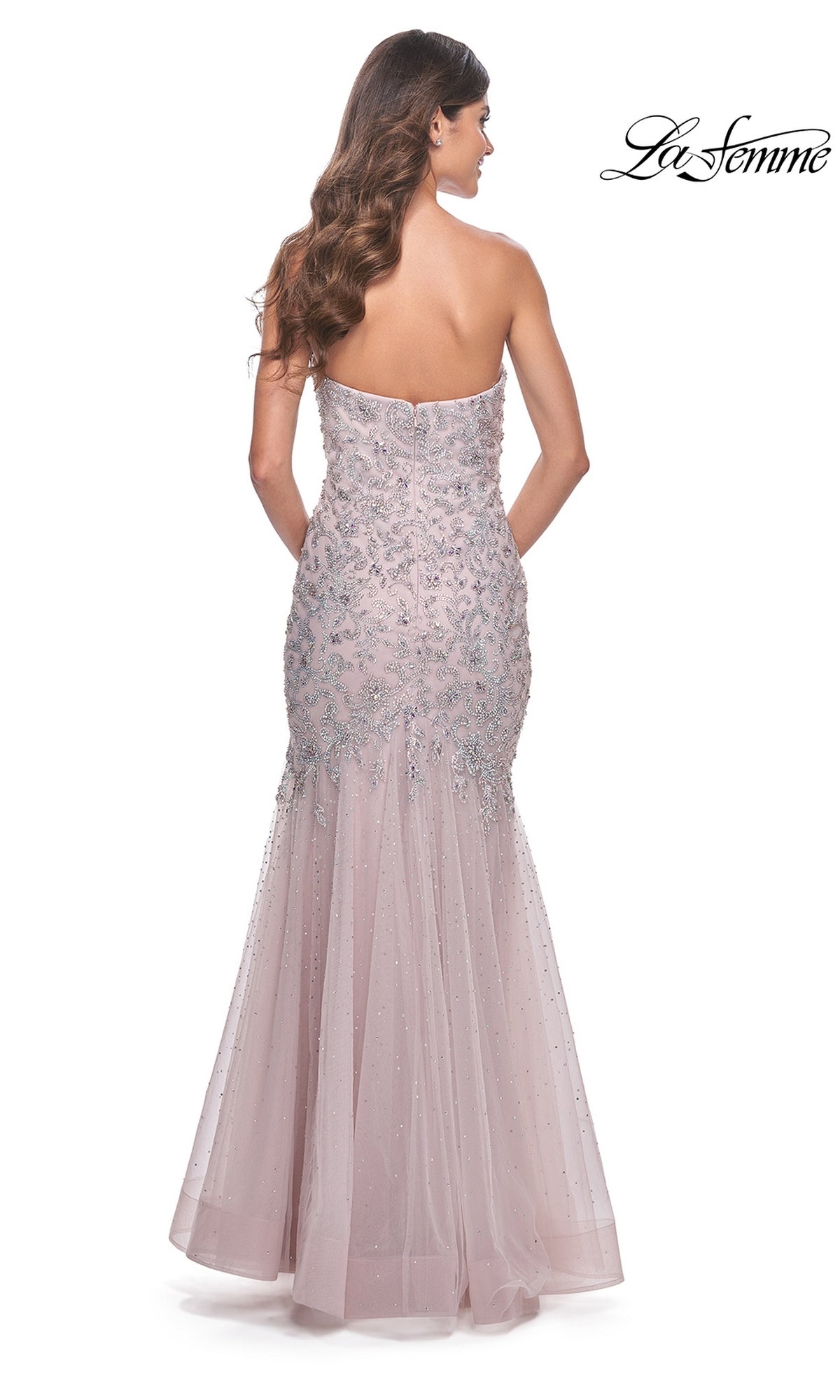 Woman wearing the La Femme Strapless Long Beaded Prom Dress 32197, a floor-length light pink mermaid gown with silver embellishments, seen from the back against a white background.