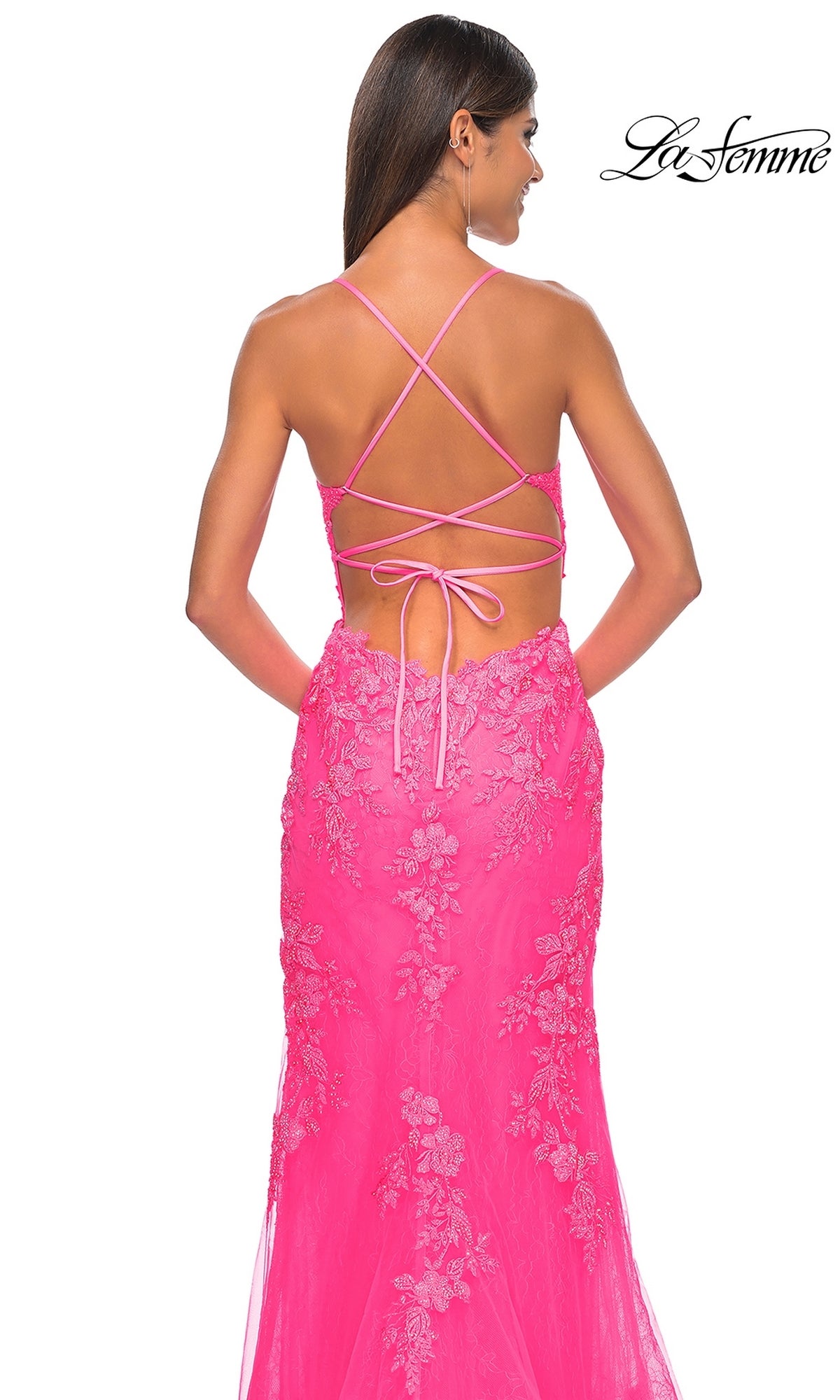 A woman faces away in the La Femme Embroidered-Lace Long Prom Dress 32205, a bright pink gown with thin crisscross straps and an open back. The