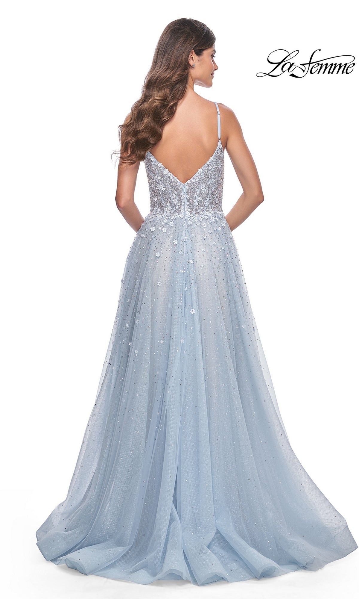 A woman with long wavy hair wears the La Femme Embellished Long A-Line Prom Dress 32215, a light blue, floor-length formal gown with thin straps, a low V-back, and sparkling embellishments. The La Femme logo appears in the top right corner.