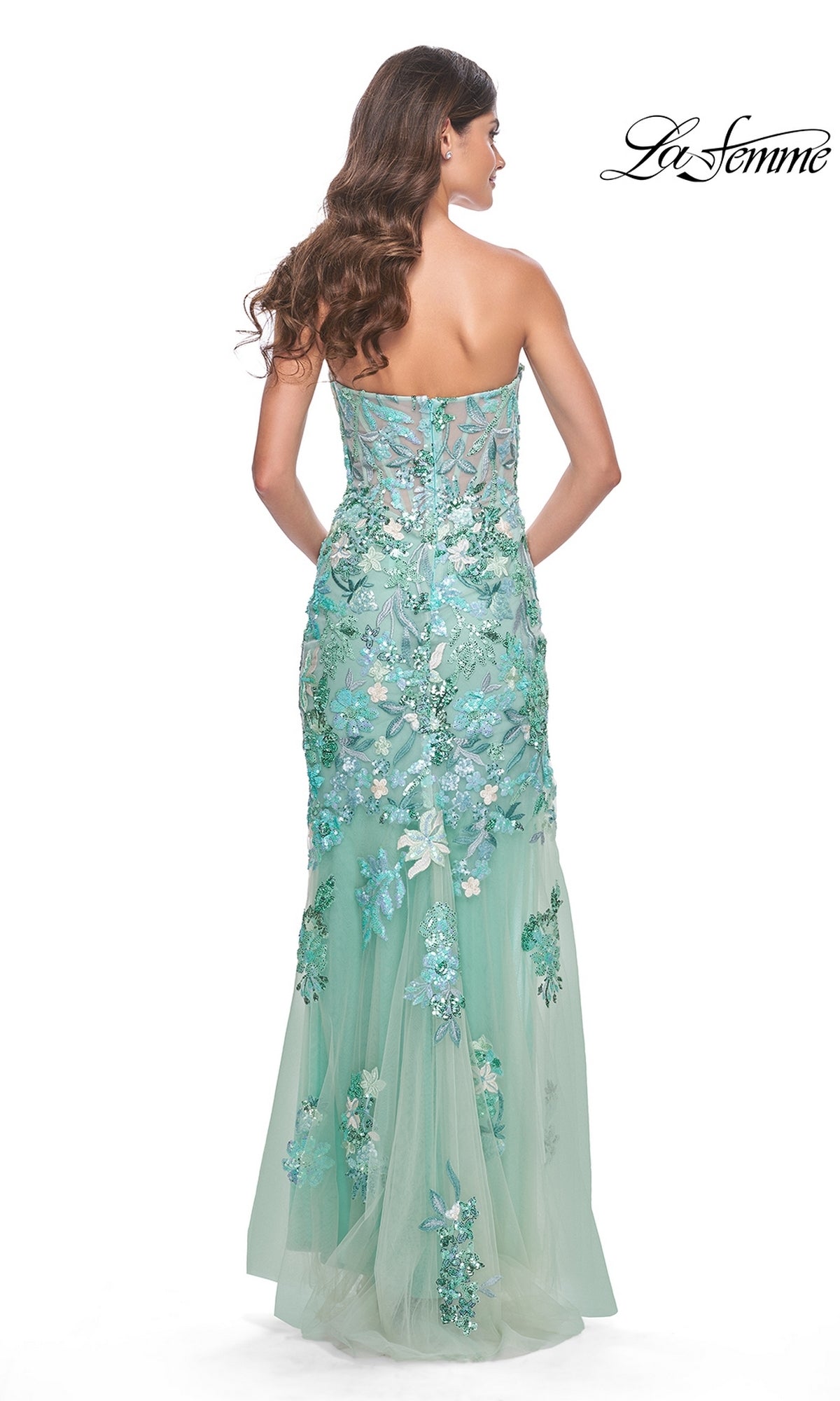 Woman in the La Femme Strapless Green Sequin Prom Dress 32252, featuring floral appliqués and sequins, stands with her back to the camera.