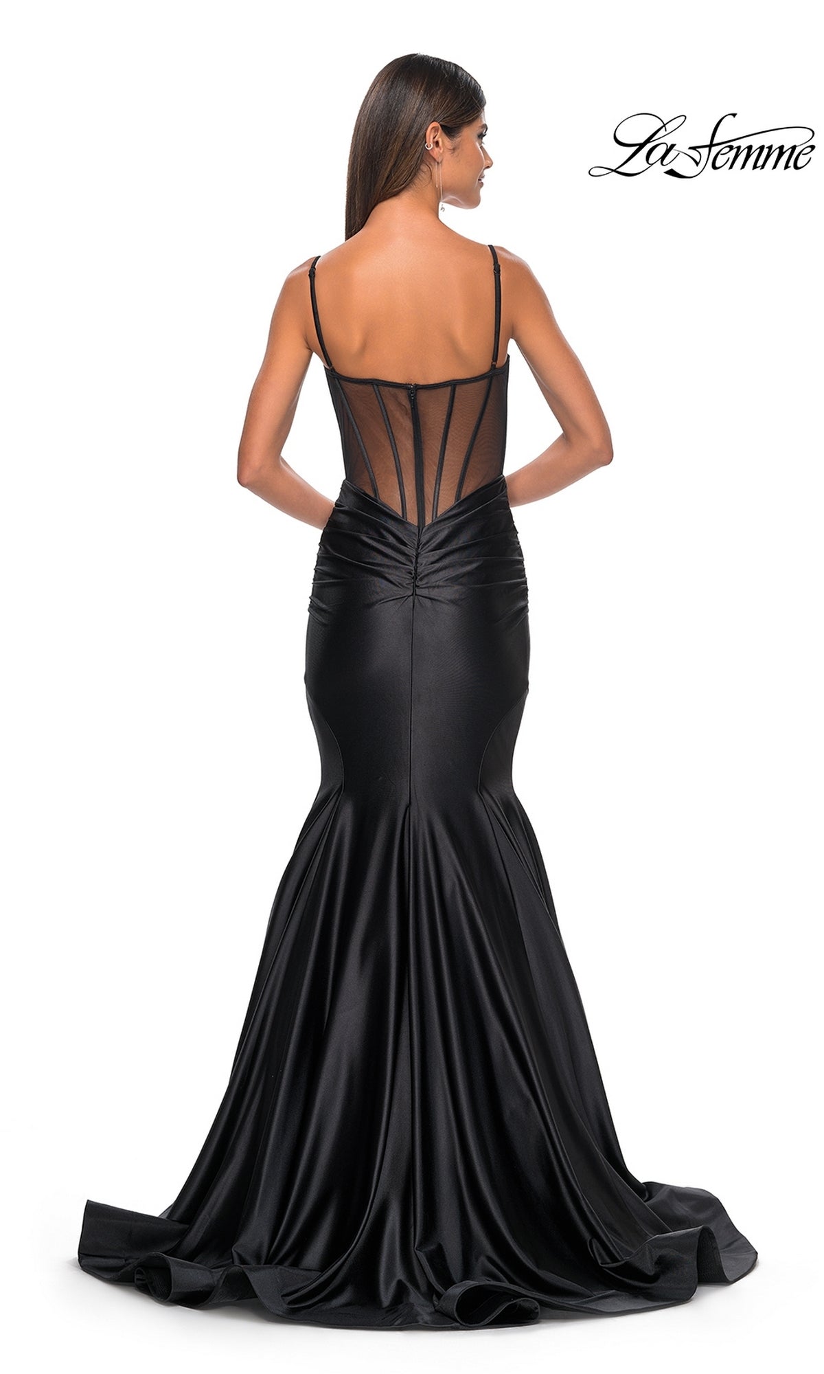 A woman wearing the La Femme Long Corset Mermaid Prom Dress 32269 in black satin, featuring a fitted bodice and sheer mesh back, stands with her back to the camera.