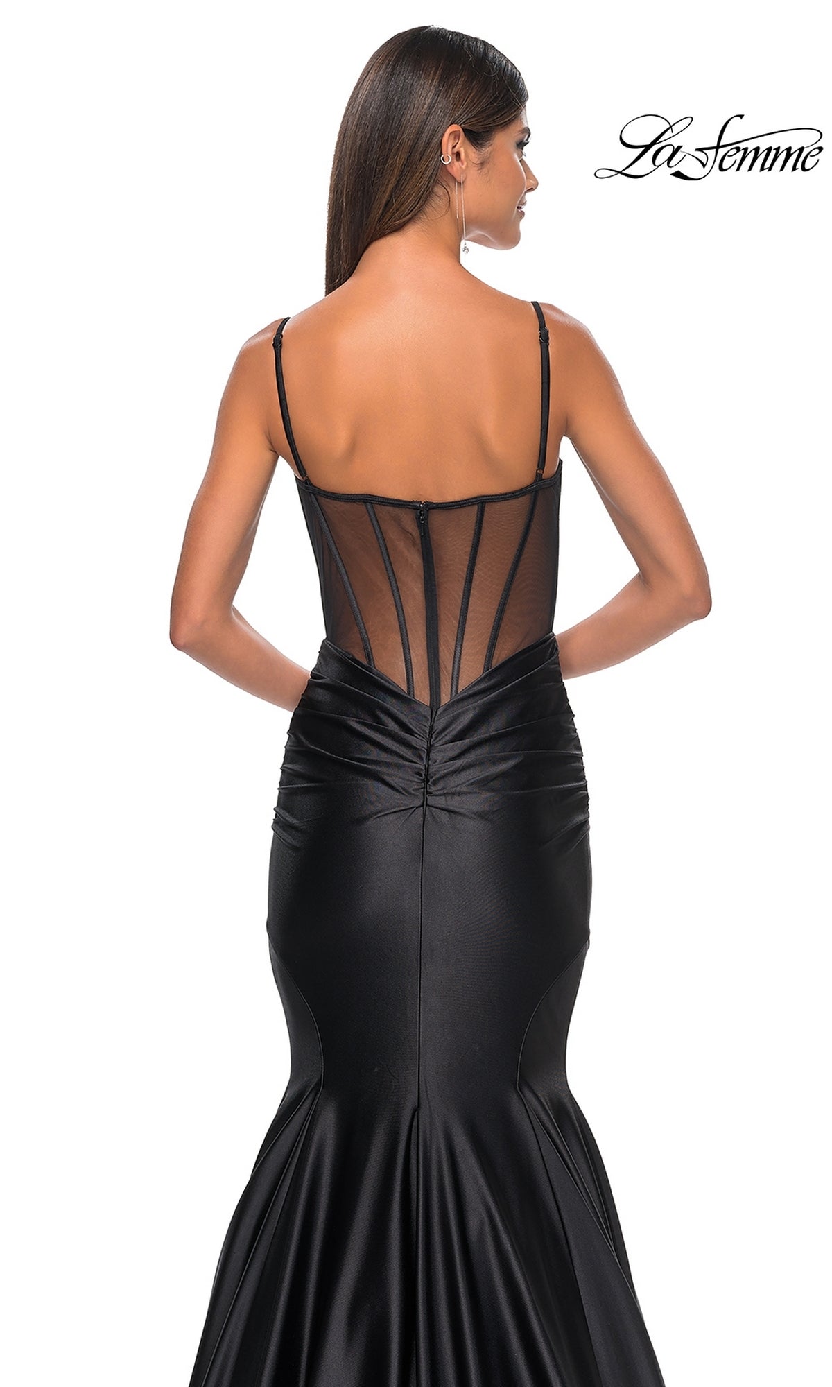 A woman wearing the La Femme Long Corset Mermaid Prom Dress 32269 in black satin, featuring a sheer mesh back and thin straps, stands with her back to the camera.