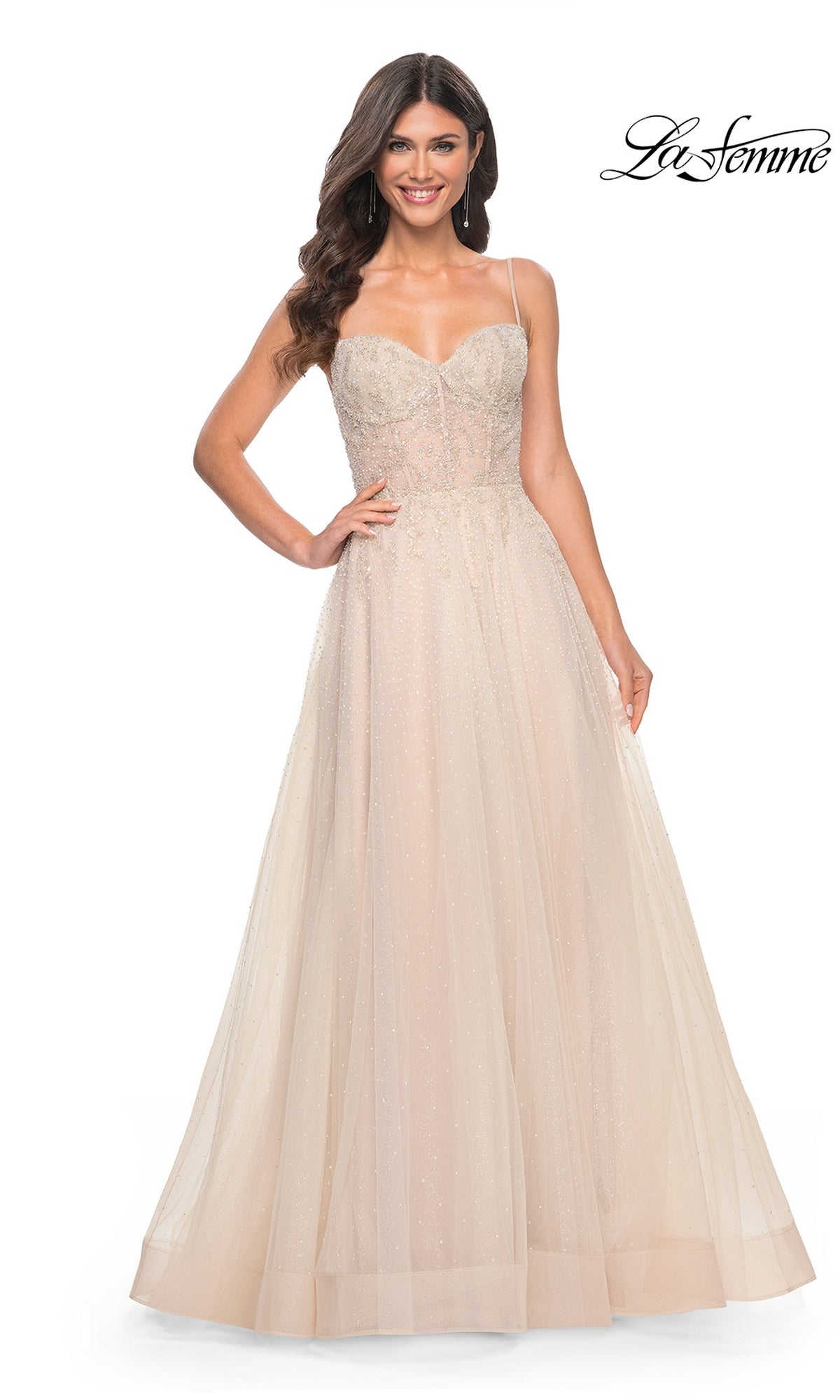 Woman wearing the La Femme Champagne Long A-Line Prom Dress 32271, featuring thin straps and a fitted embellished bodice, standing and smiling in front of a white background.
