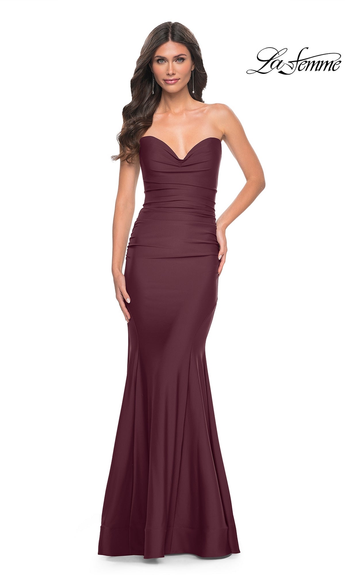 A woman wears the La Femme Strapless Lace-Up Long Prom Dress 32289 in maroon, featuring a fitted bodice and subtle mermaid skirt. The