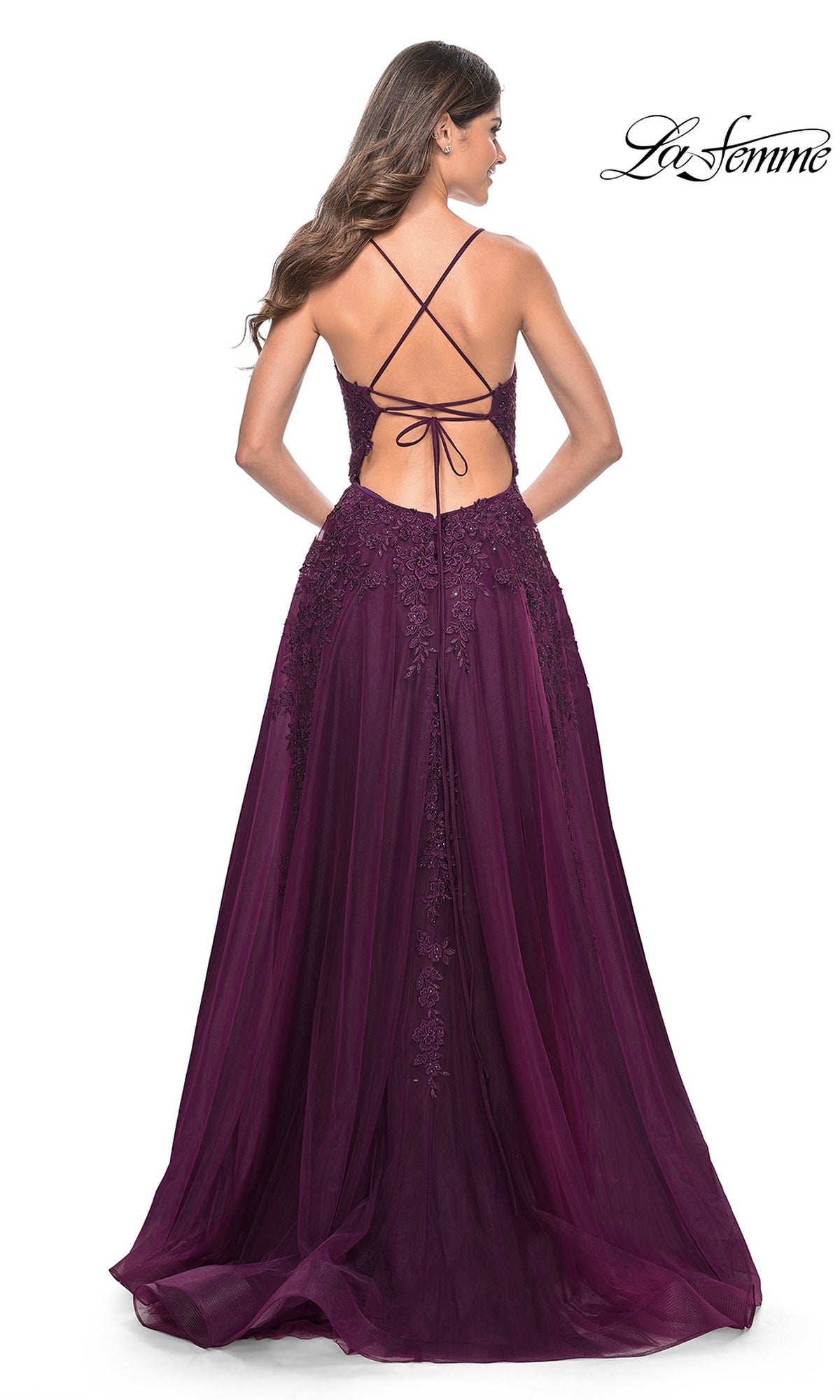 A woman in the La Femme Long Lace A-Line Prom Dress 32303, featuring a deep purple hue, lace bodice, open lace-up back, and flowing tulle skirt—an elegant choice for any formal occasion.