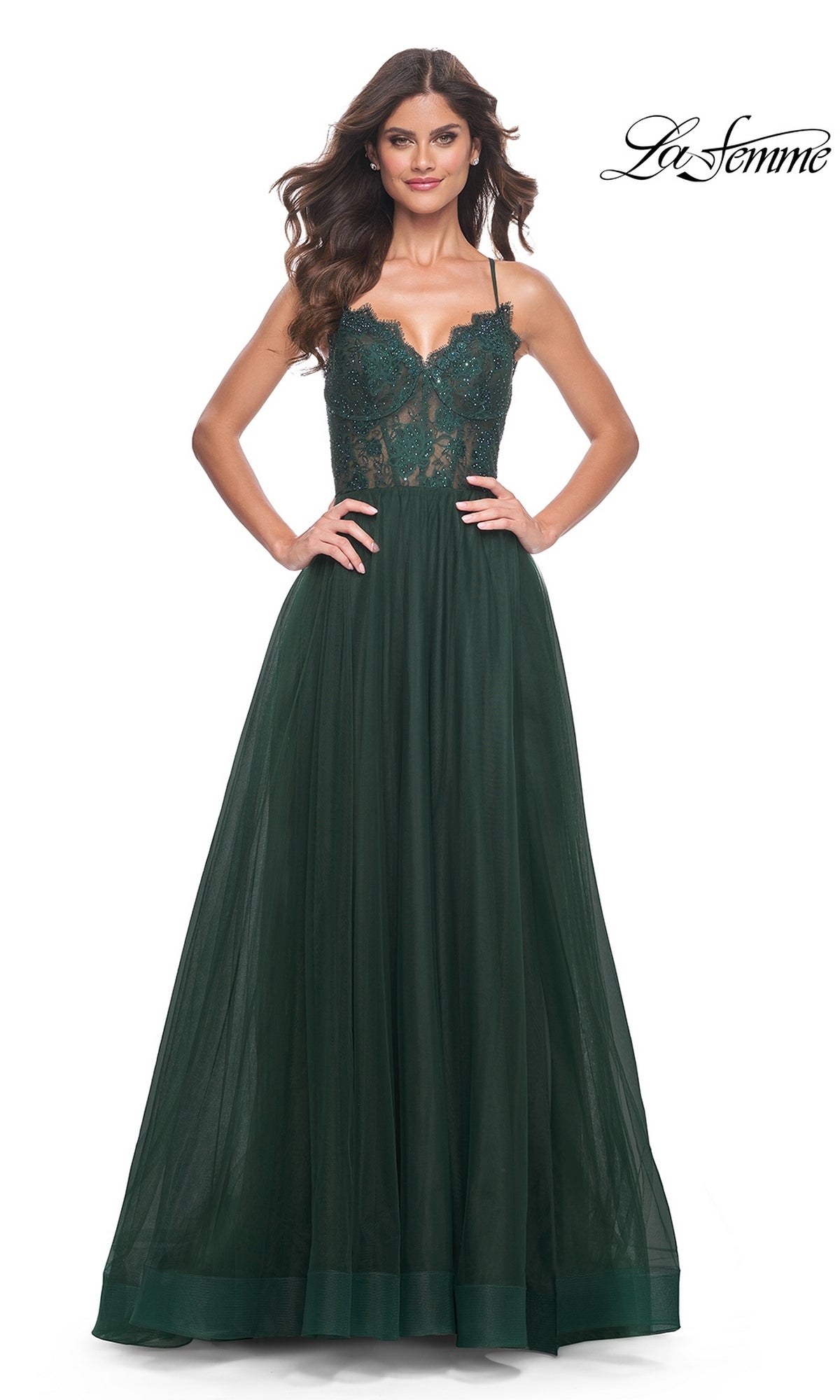 A woman in the La Femme Lace-Bodice Long A-Line Prom Dress 32306, featuring a dark green fitted lace bodice and tulle skirt, stands with hands on hips against a white background.