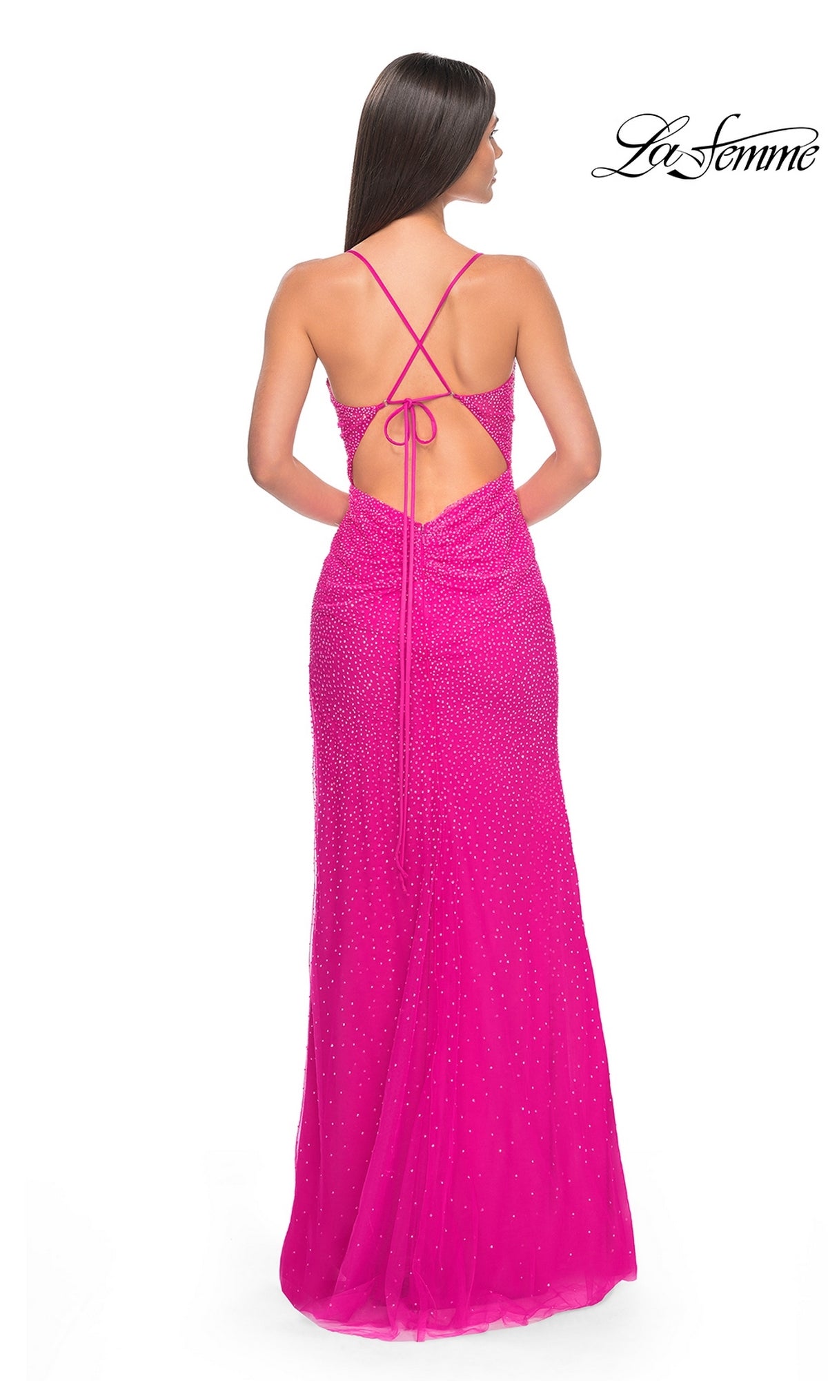 A woman stands facing away in the La Femme Cut-Out Long Beaded Prom Dress 32328—a bright pink, floor-length gown with thin crisscross back straps and subtle bead embellishments.