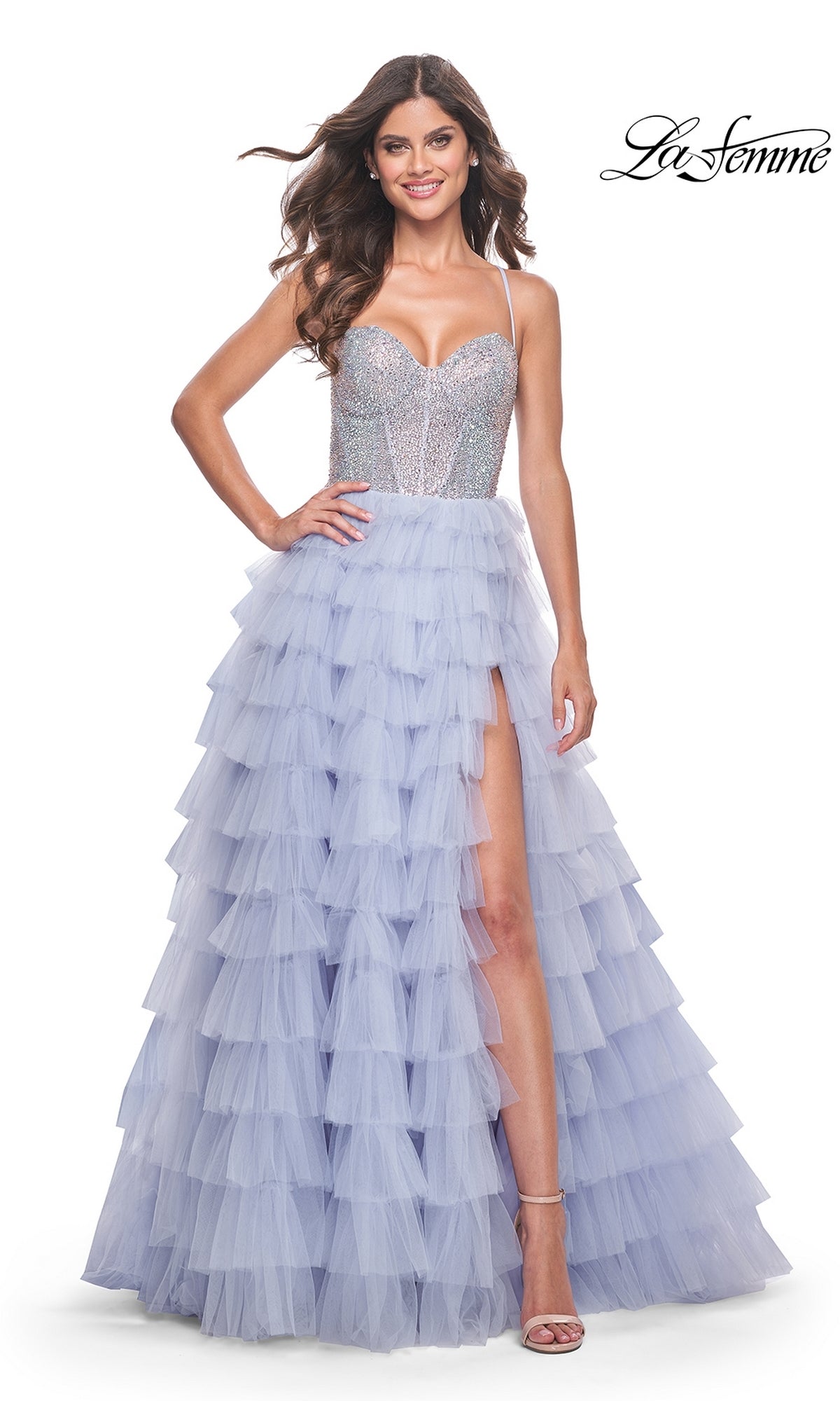 A woman stands and smiles in the La Femme Long Tiered A-Line Prom Dress 32335, featuring a silver sequin bodice with spaghetti straps and a layered lavender tulle skirt with a thigh-high side slit. “La Femme” logo in the top right corner.