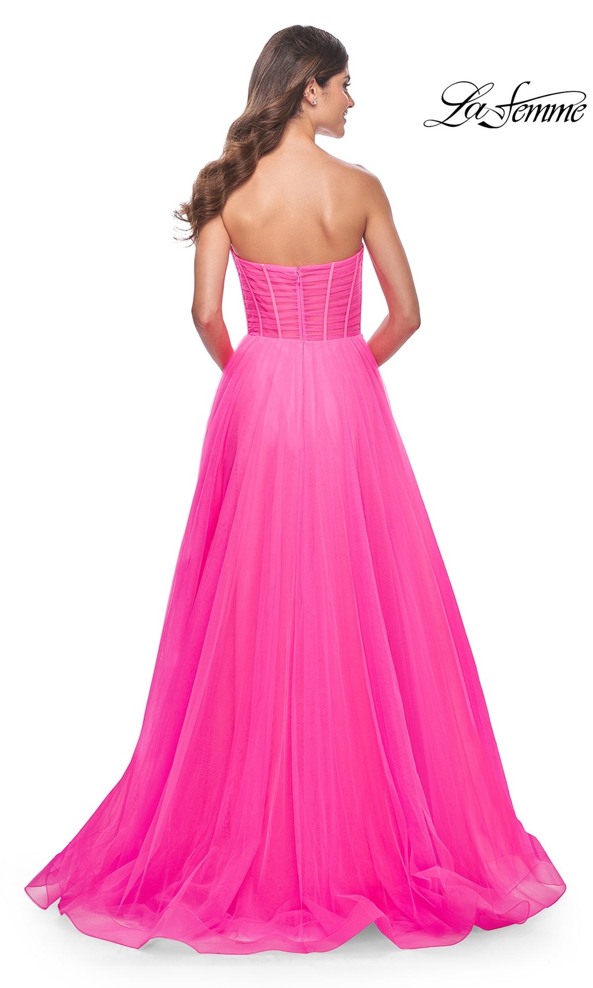 A woman faces away in a neon pink, floor-length La Femme Long Pink Corset A-Line Prom Dress 32341 with a fitted bodice and flowing skirt. The
