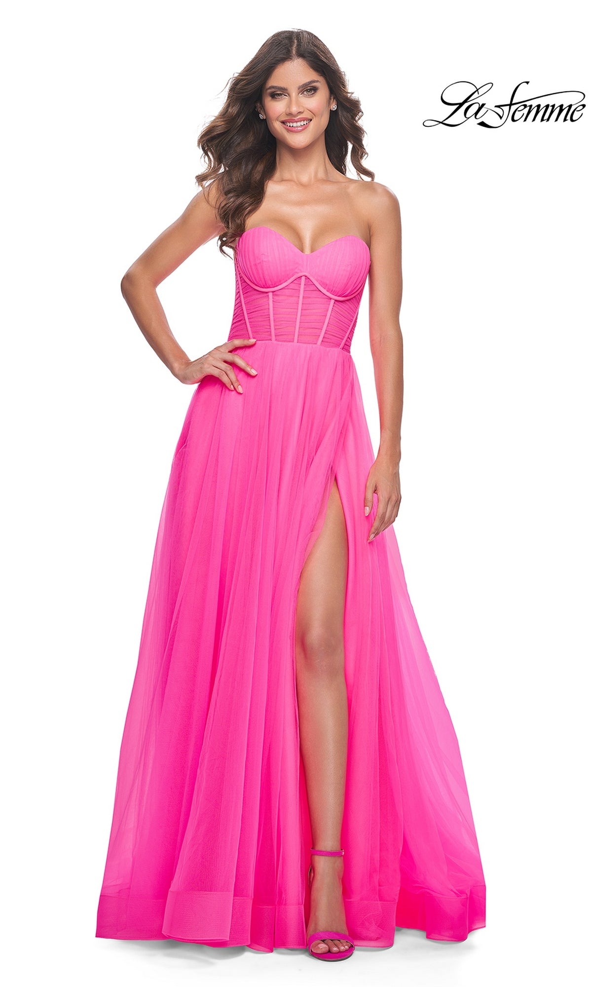 A woman smiles in the La Femme Long Pink Corset A-Line Prom Dress 32341, featuring a fitted bodice and high slit in neon pink. The La Femme logo is visible in the top right corner, highlighting the dress’s elegant design.