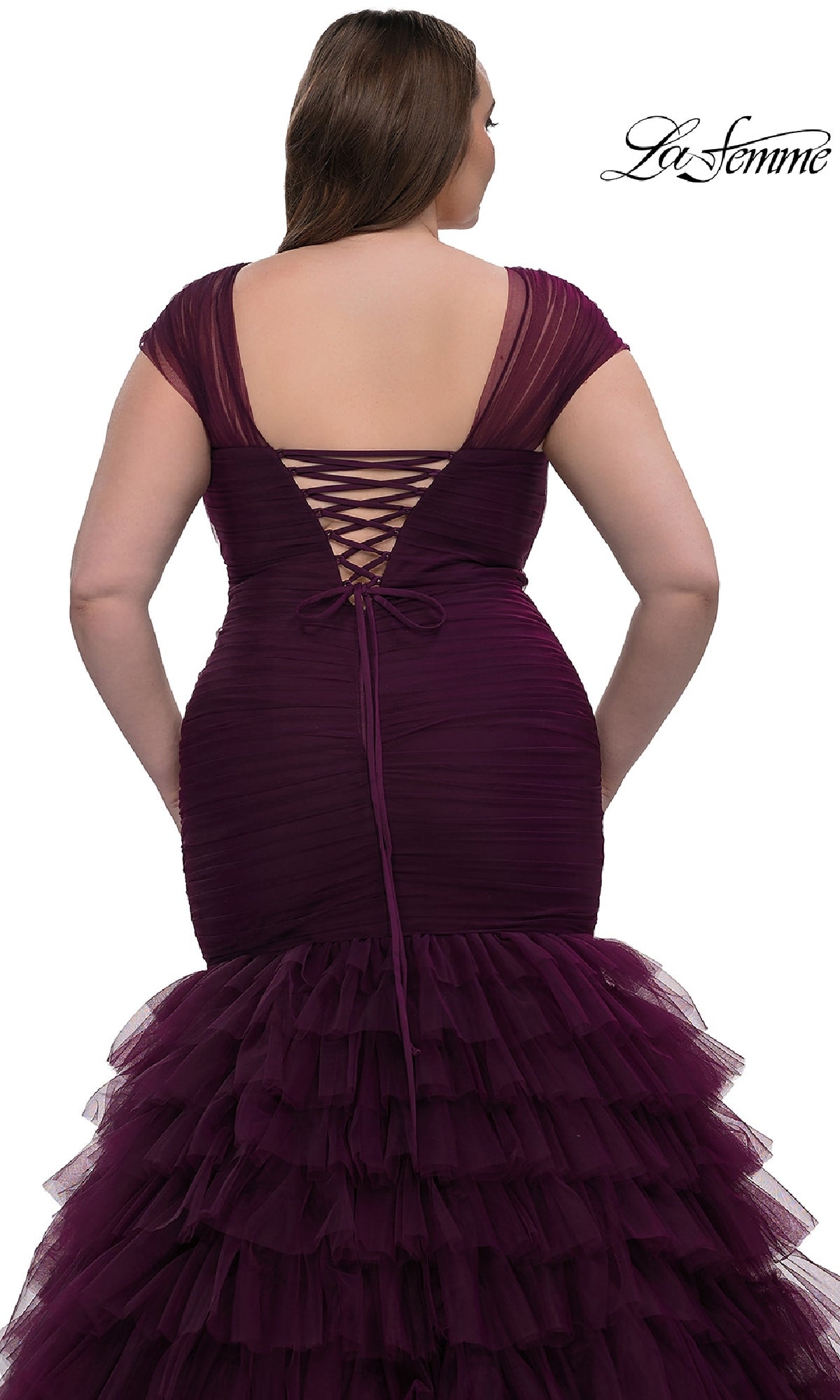 A woman is shown from behind wearing the La Femme 32389 plus-size long mermaid prom dress in deep purple, featuring a ruched silhouette, lace-up back, and tiered tulle skirt.