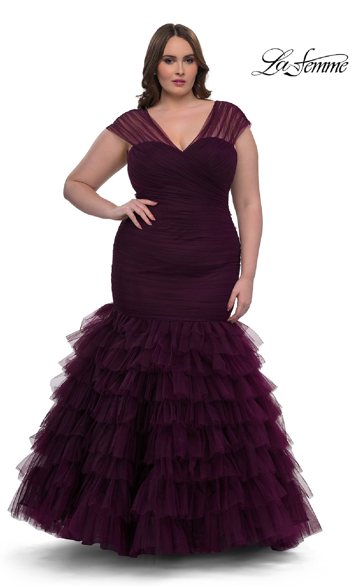A woman models the La Femme 32389, a plus-size long mermaid prom dress in deep purple with sheer cap sleeves, a fitted ruched bodice, and a tiered tulle skirt. The La Femme logo appears in the top right corner.