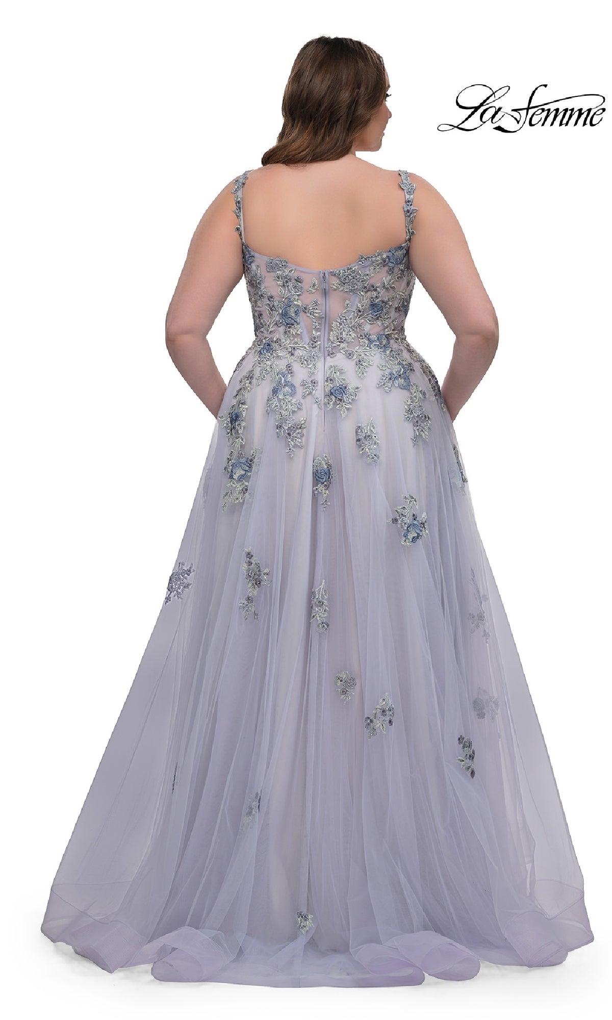 A woman is shown from the back wearing the La Femme 32412 Long Plus-Size Prom Ball Gown, a light lavender dress with floral appliqués, a sheer overlay, thin straps, corset bodice, and delicate lace embroidery for an elegant look.
