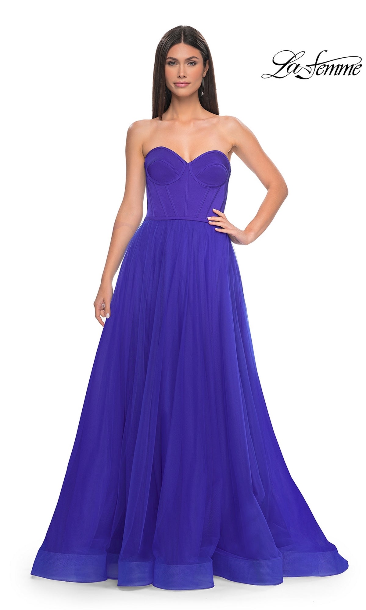 A woman models the Strapless Long Tulle Prom Dress: La Femme 32424, featuring a fitted bodice and flowing floor-length royal blue skirt, standing against a plain white background.