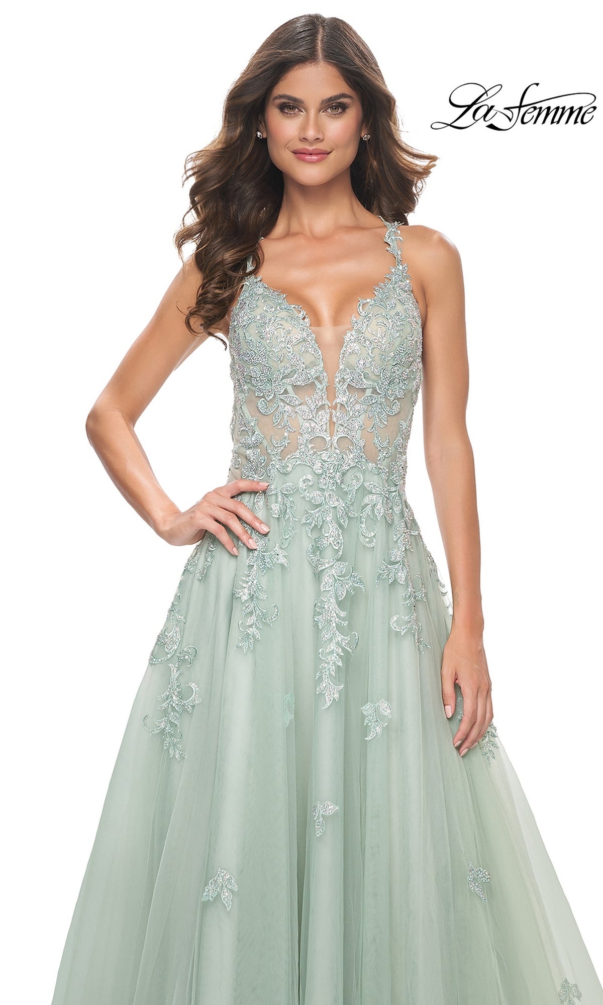 A woman in the Sheer-Waist Long A-Line Prom Dress (La Femme 32438)—a light green, sleeveless, embroidered lace gown with a deep V-neckline—stands before a white background. The La Femme logo is shown in the top right corner.