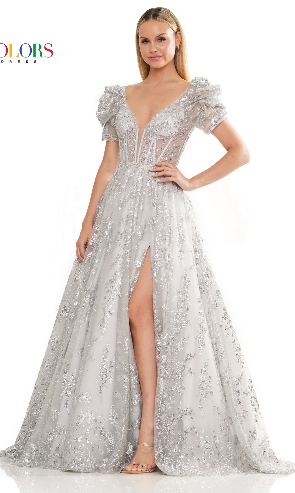 A woman wears the Short-Sleeve Long Glitter A-Line Prom Dress 3243—silver, floor-length, with sequin details, sheer short sleeves, and a high slit. She stands facing forward with one hand on her hip.