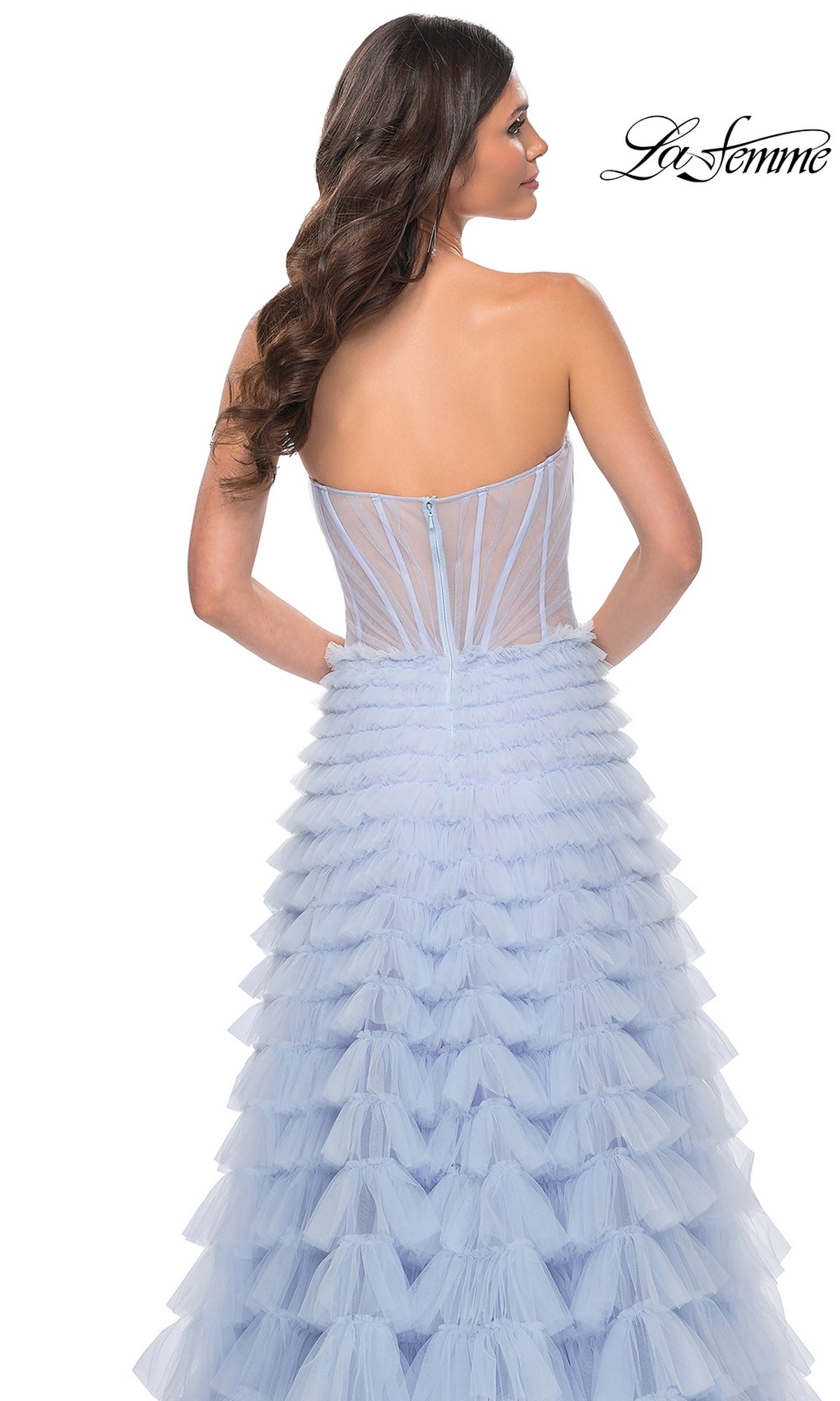 A woman models the Long Ruffled A-Line Prom Ball Gown: La Femme 32447, featuring a strapless light blue tiered tulle skirt and fitted sheer corset bodice, shown from the back with the
