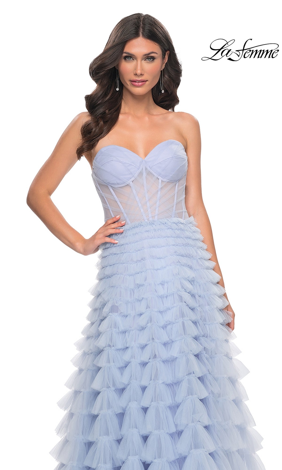 A woman stands against a white background wearing the La Femme 32447 long ruffled A-line prom ball gown, featuring a strapless light blue tulle design with a fitted sheer bodice and layered skirt.