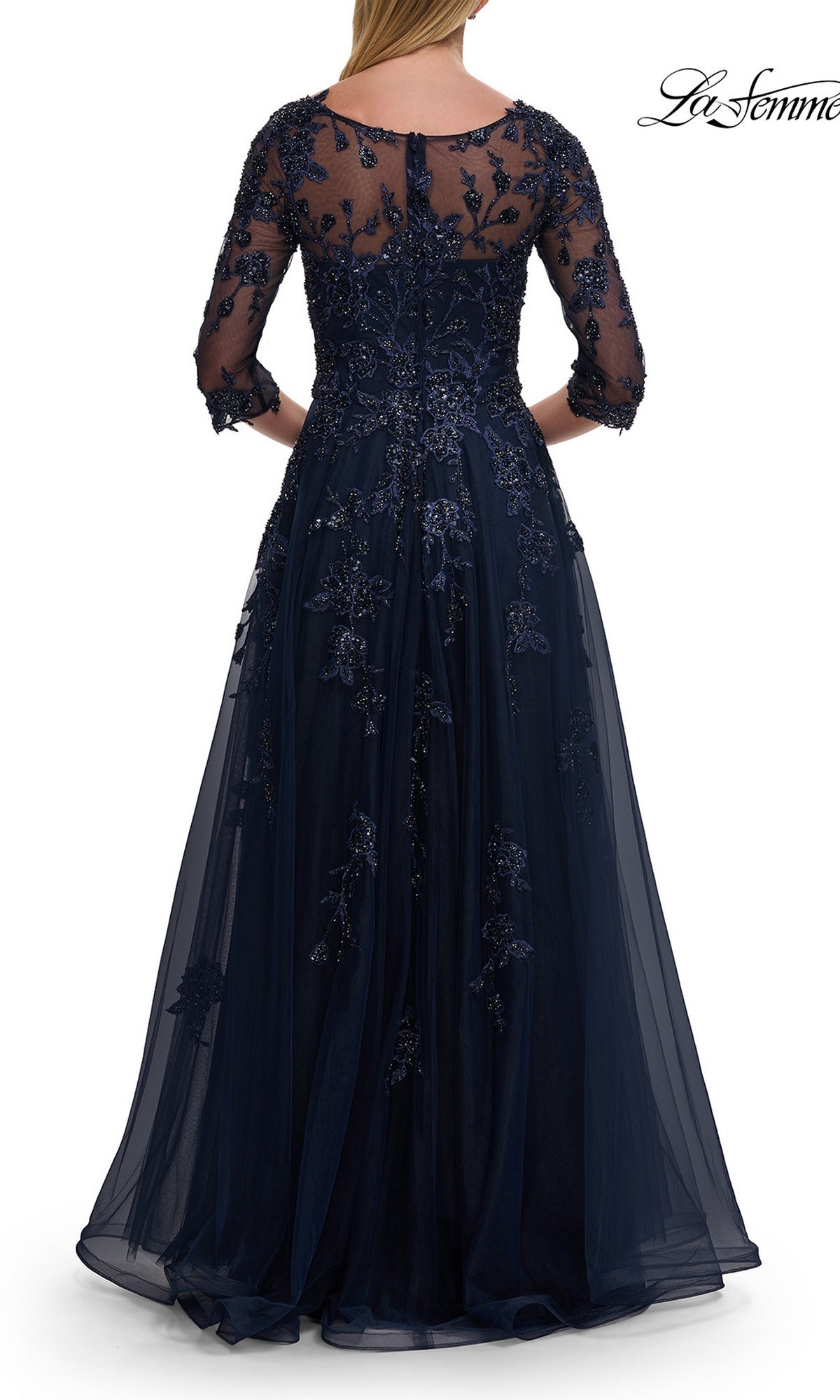 A woman is seen from the back wearing the La Femme 32538, an A-line navy blue tulle formal dress with sheer sleeves and delicate beaded lace appliques.