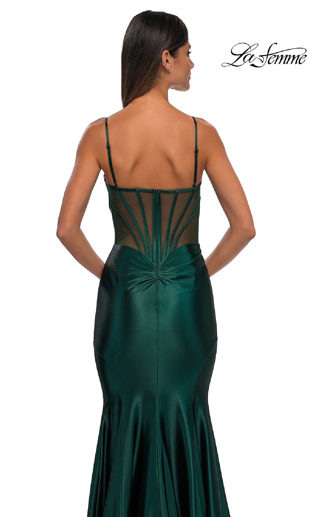 Woman in the Long Corset Mermaid Prom Dress: La Femme 32555—a dark green satin gown with thin straps and a sheer back panel with geometric lines, perfect for prom or any formal occasion, shown standing against a white background.