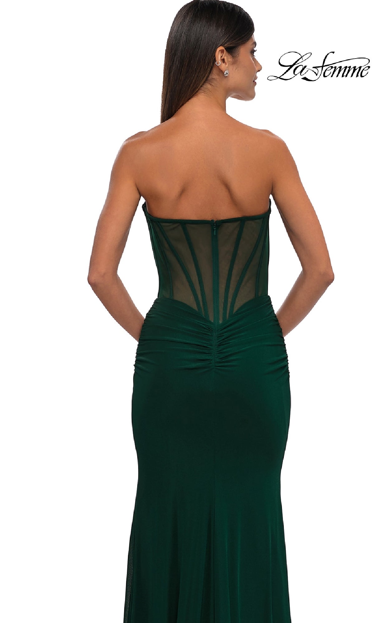 A woman in the La Femme 32734 cut-out long strapless prom dress, featuring a sheer corset back and ruched details, stands facing away to elegantly highlight the allure of this dark green evening gown.