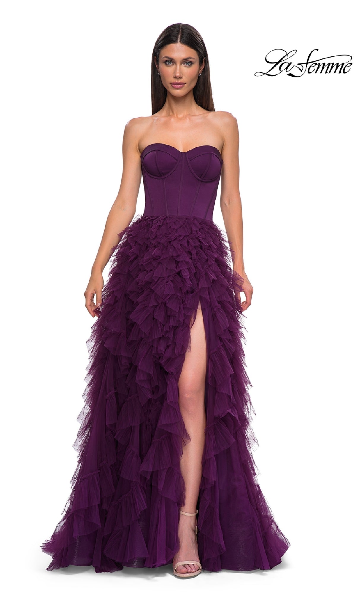 A woman wears the Strapless Long Ruffled Prom Dress: La Femme 32760, featuring a corset-style bodice, thigh-high slit, and purple tulle A-line skirt, standing against a white background.