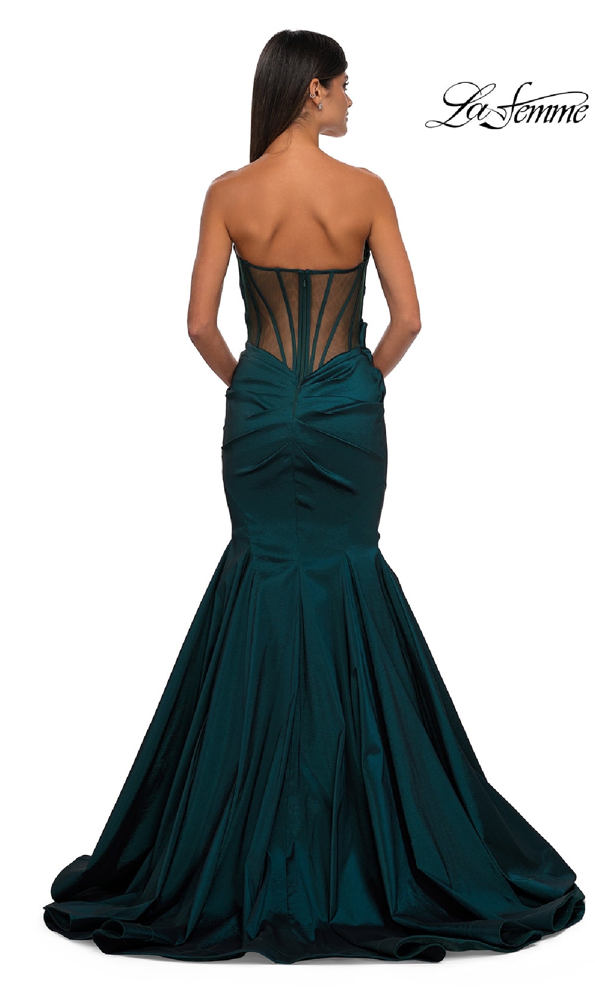 A woman with long, straight hair wears the La Femme 32791 strapless long mermaid prom dress in dark green, featuring a sheer black corset back and ruched details, standing against a white background.
