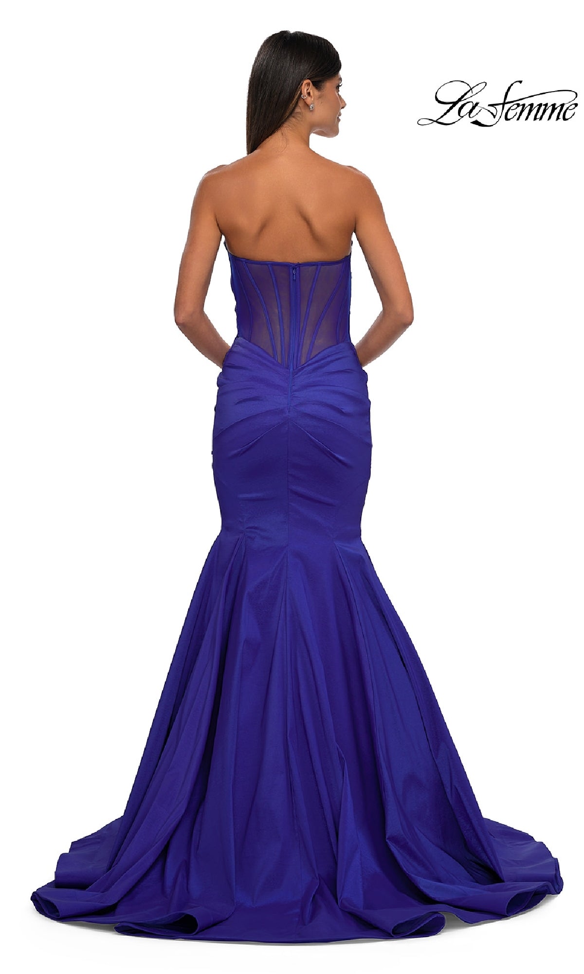A woman models the La Femme 32791: a strapless long mermaid prom dress in royal blue with a sheer panel back and flared train, showcasing its elegance as she faces away from the camera.