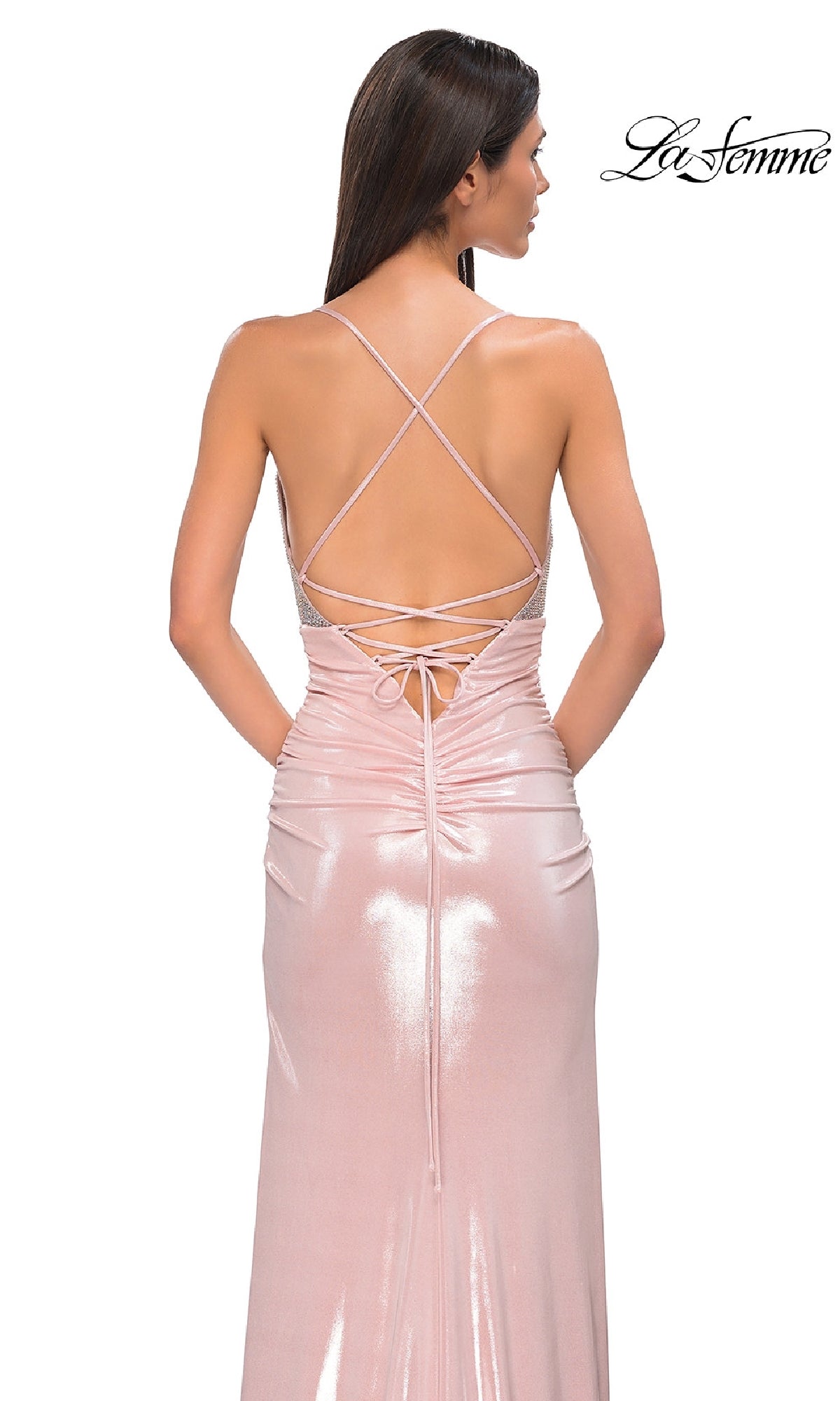 A woman faces away from the camera in a shiny, light pink Strappy Long Jersey Prom Dress: La Femme 32793, featuring a floor-length silhouette and strappy open back for an elegant look.